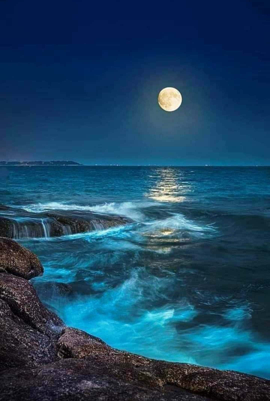 月光反射在夜間拍打岩石海岸的海浪上。