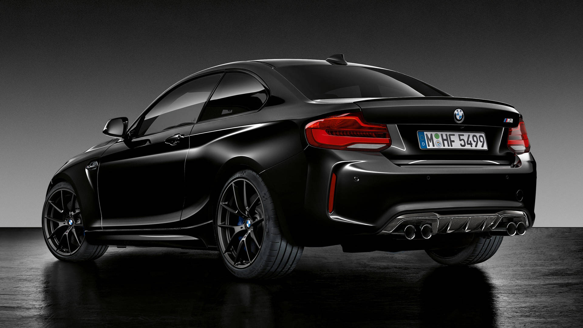 美麗的黑色BMW M2 壁紙 — 一輛時尚的黑色BMW M2雙門轎跑車，從後方四分之三角度展示，帶有發光的紅色尾燈和四出排氣管，位於深色工作室地板上。