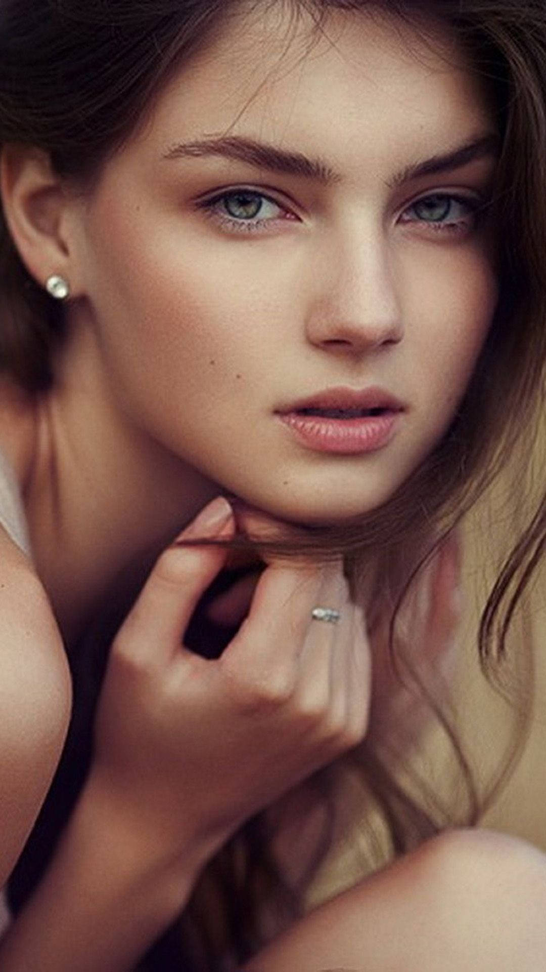 年輕女性，綠色眼睛，棕色頭髮，手指戴戒指觸碰下巴。