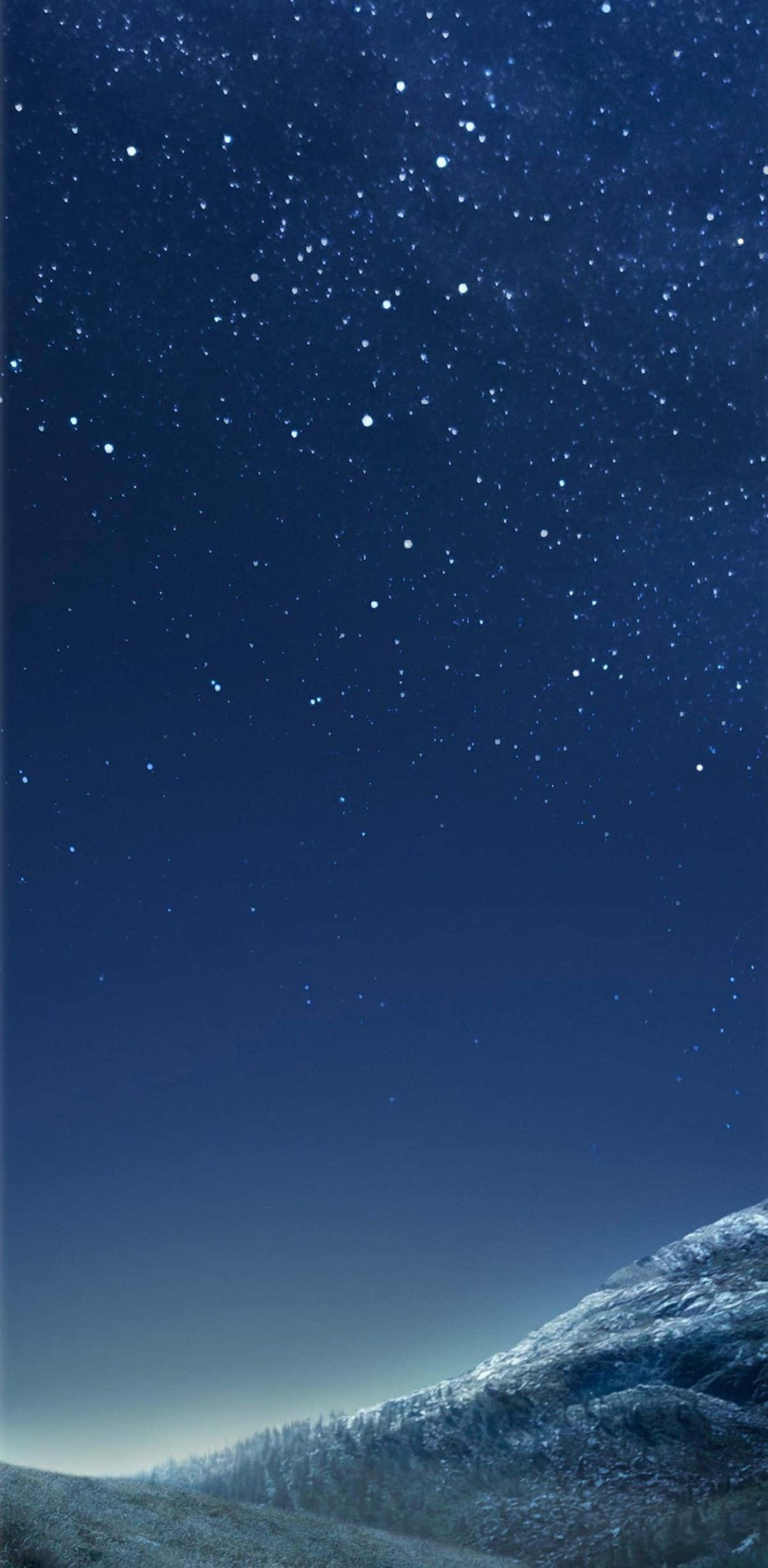 美麗銀河主題手機壁紙 壁紙 — 在深靛藍色的天空下，星空籠罩著積雪的山脊。
