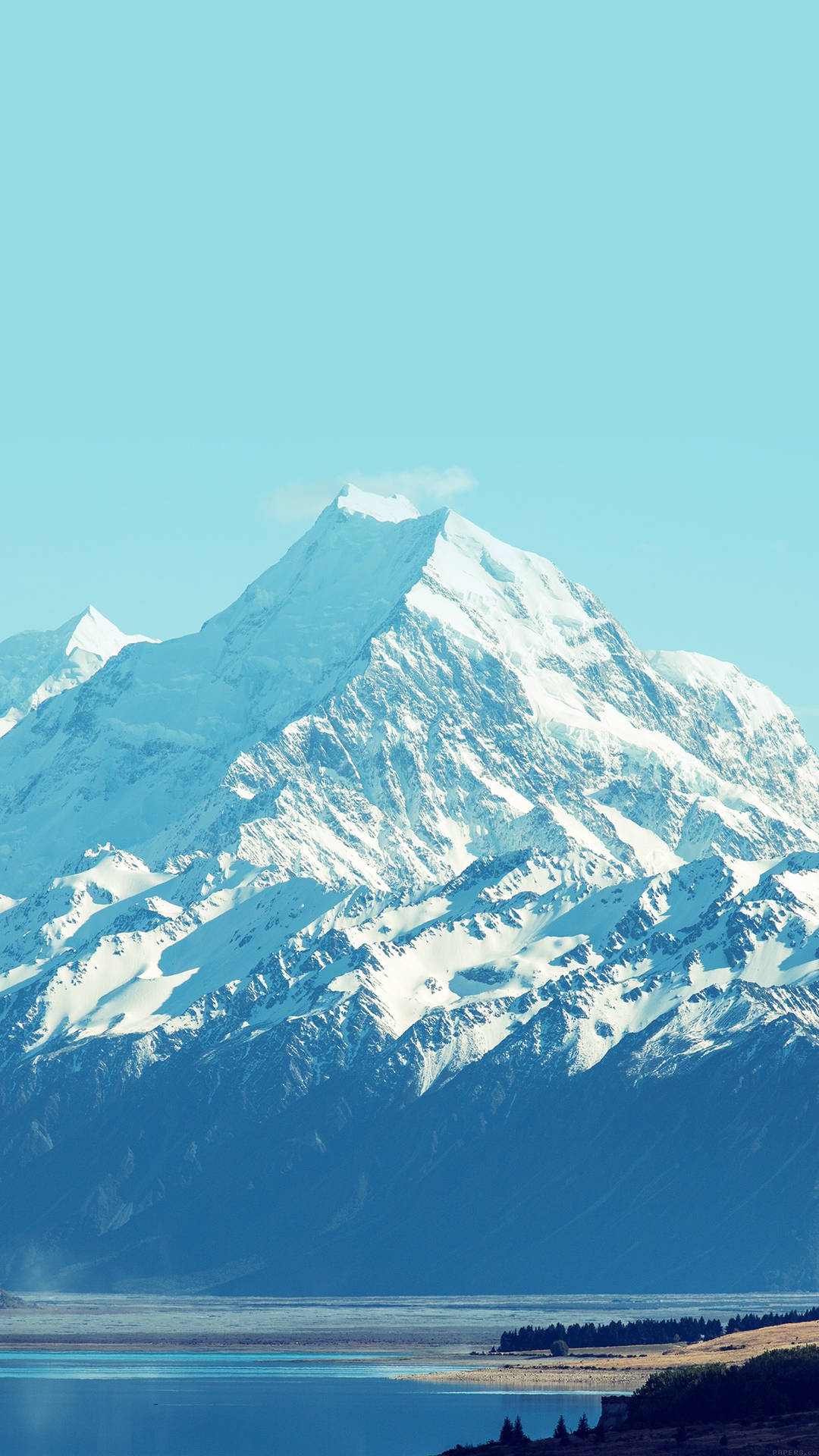 雪山峰俯瞰著晴朗天空下寧靜的藍色湖泊。