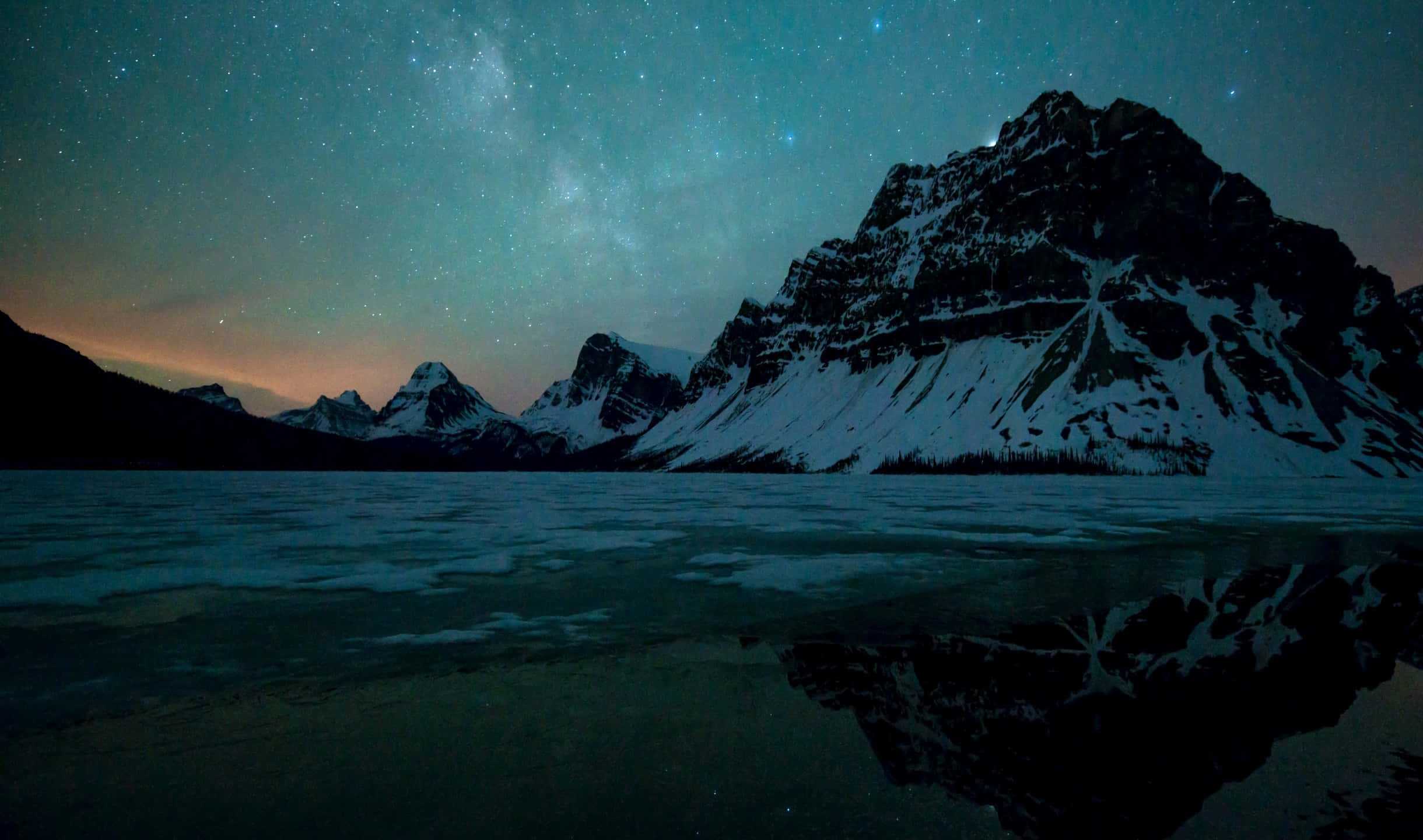 群山倒影於星夜湖面 壁紙 — 積雪的山峰在繁星點點的夜空下倒映，銀河在平靜的湖面上拱起。
