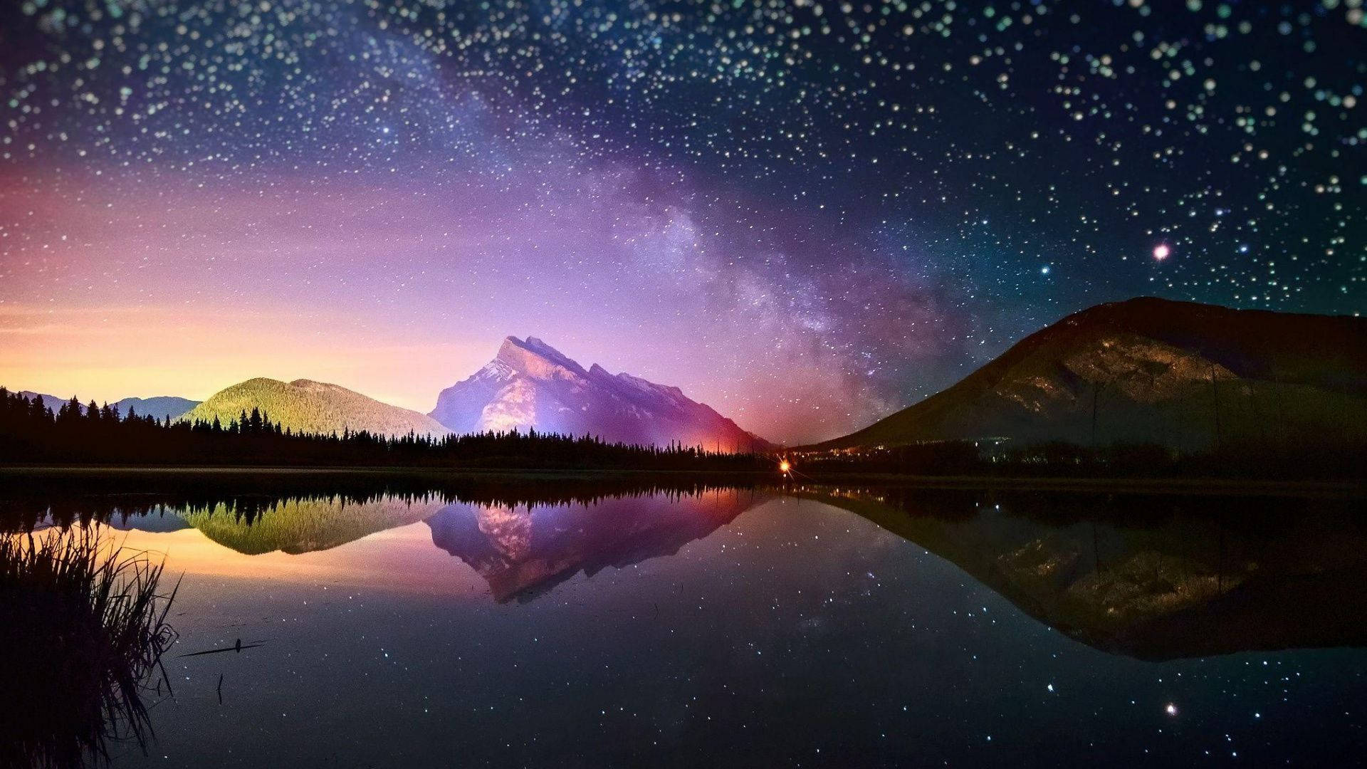 雪覆山巒在星空下倒映在夜晚平靜的湖面上。