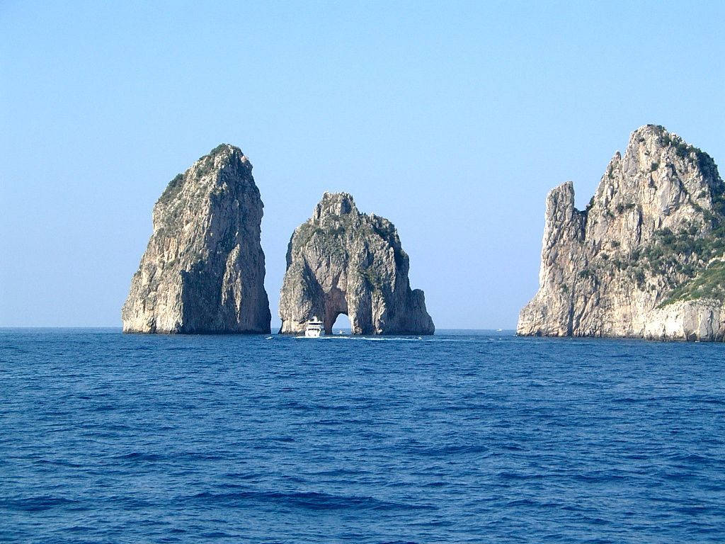 船隻穿過卡布里島法拉廖尼岩石在藍色海中的拱門。
