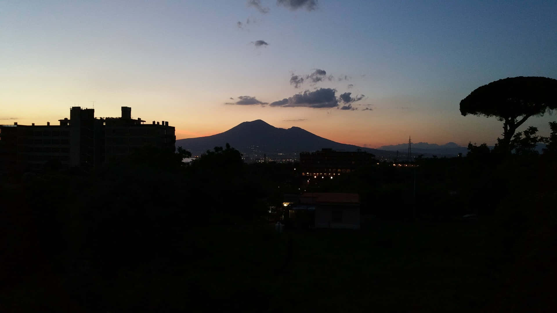 維蘇威火山在暮色天空中形成剪影，位於城市上空，帶有橙色地平線。
