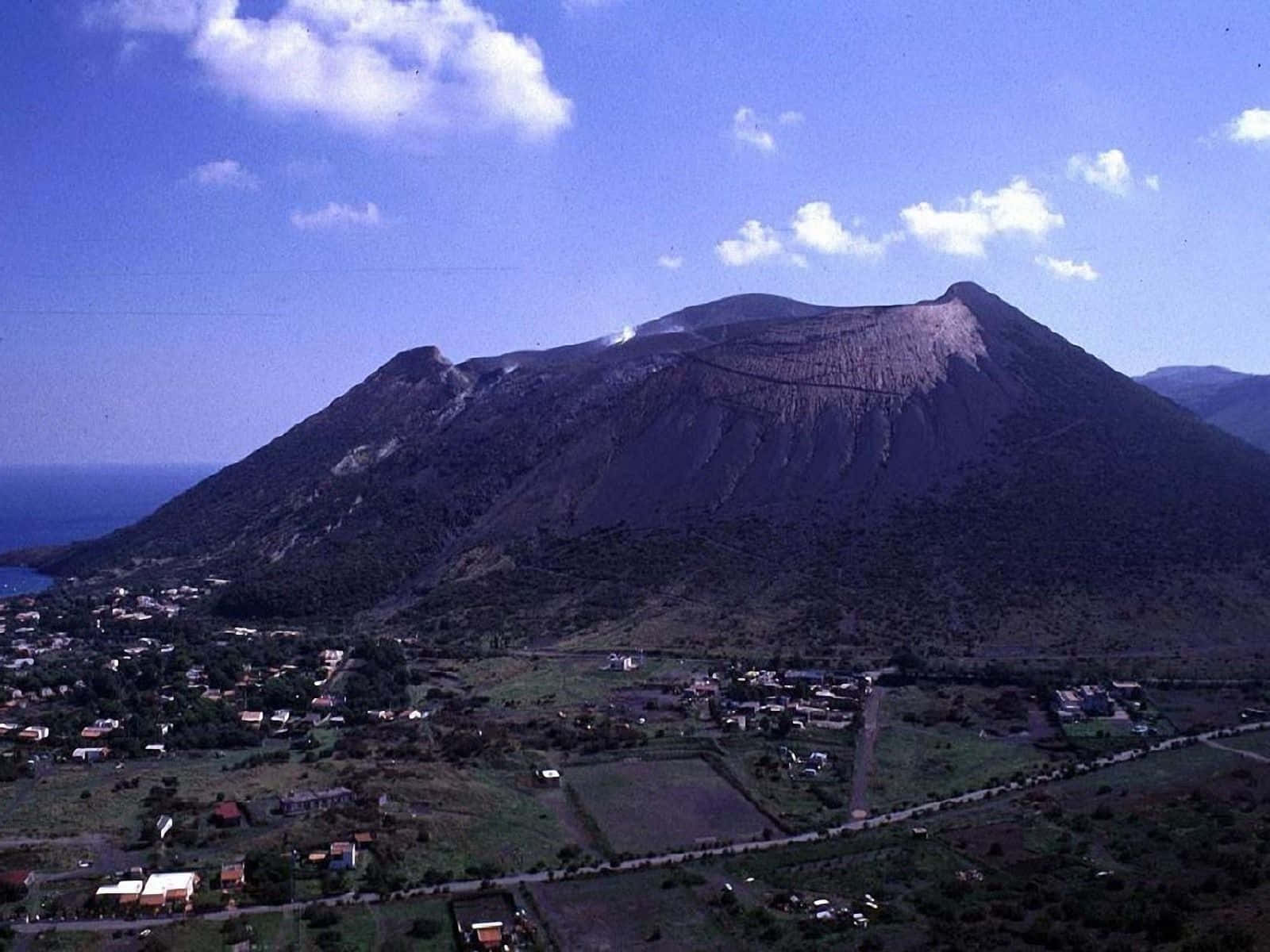 藍天白雲下，火山下方有一個沿海小鎮。