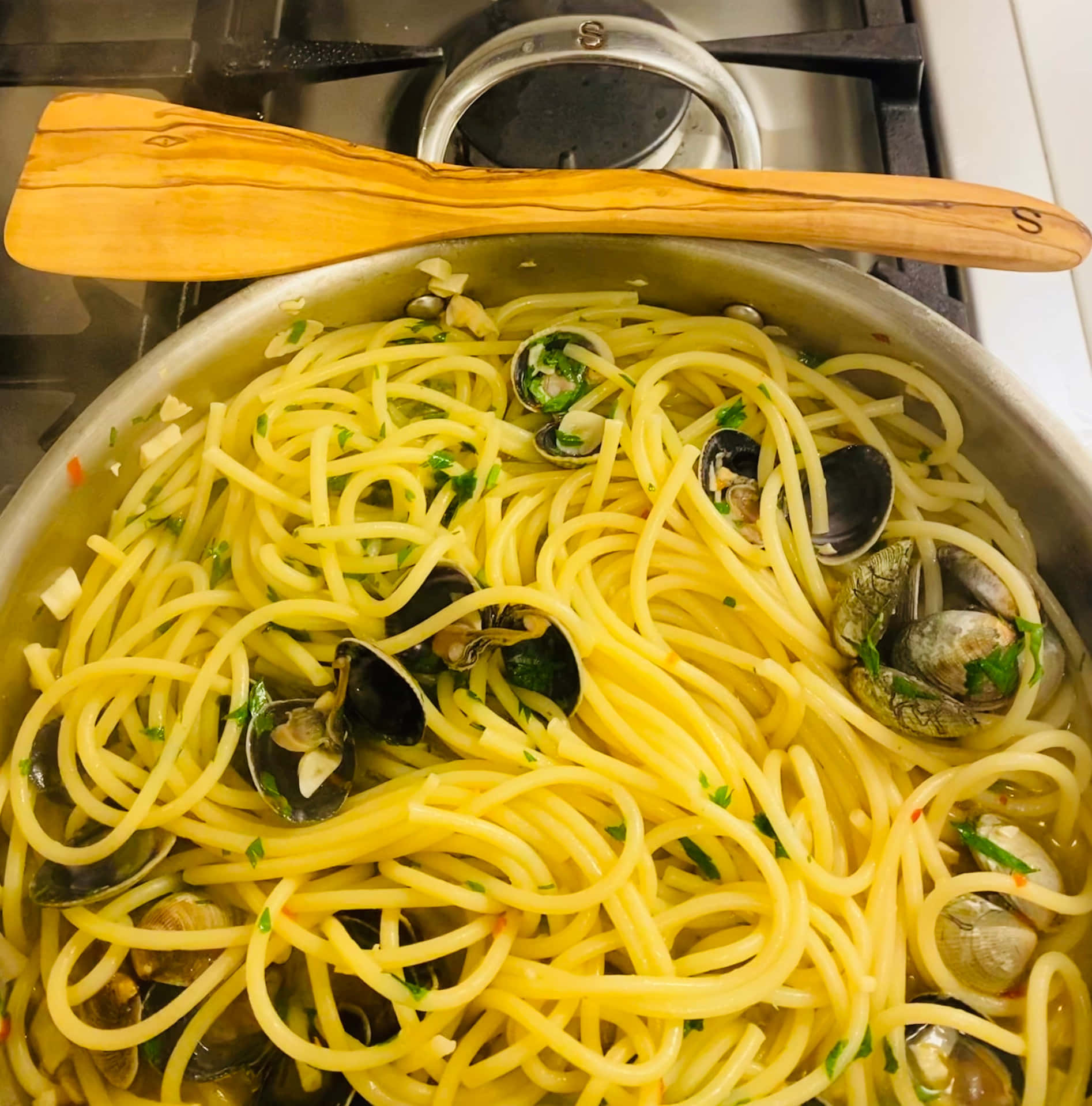 蜆肉香草意大利粉在鍋中，爐灶上有一隻木勺。