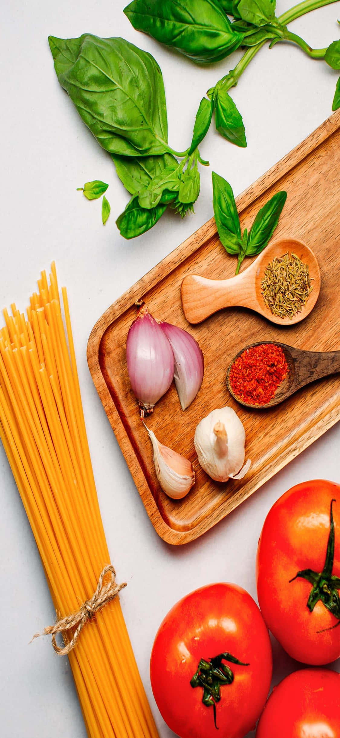 義大利麵食材 iPhone X 義大利麵背景 壁紙 — 新鮮意粉材料包括番茄、羅勒、大蒜和香料，整齊排列在木板上，背景為純白色。