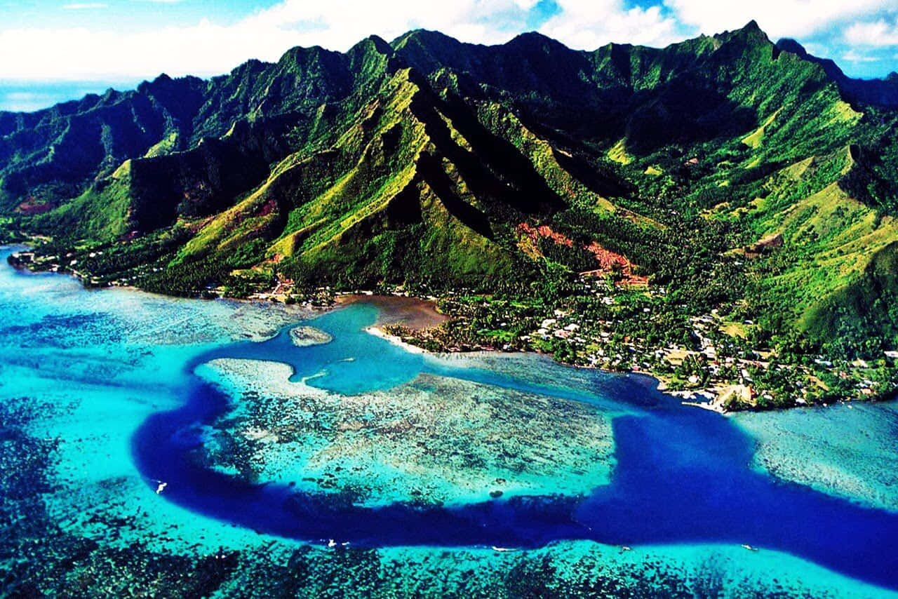 Jamaican Island 桌布 壁紙 — 翠綠山巒與充滿活力的綠松石珊瑚礁及一個小沿海村莊交匯的鳥瞰圖。