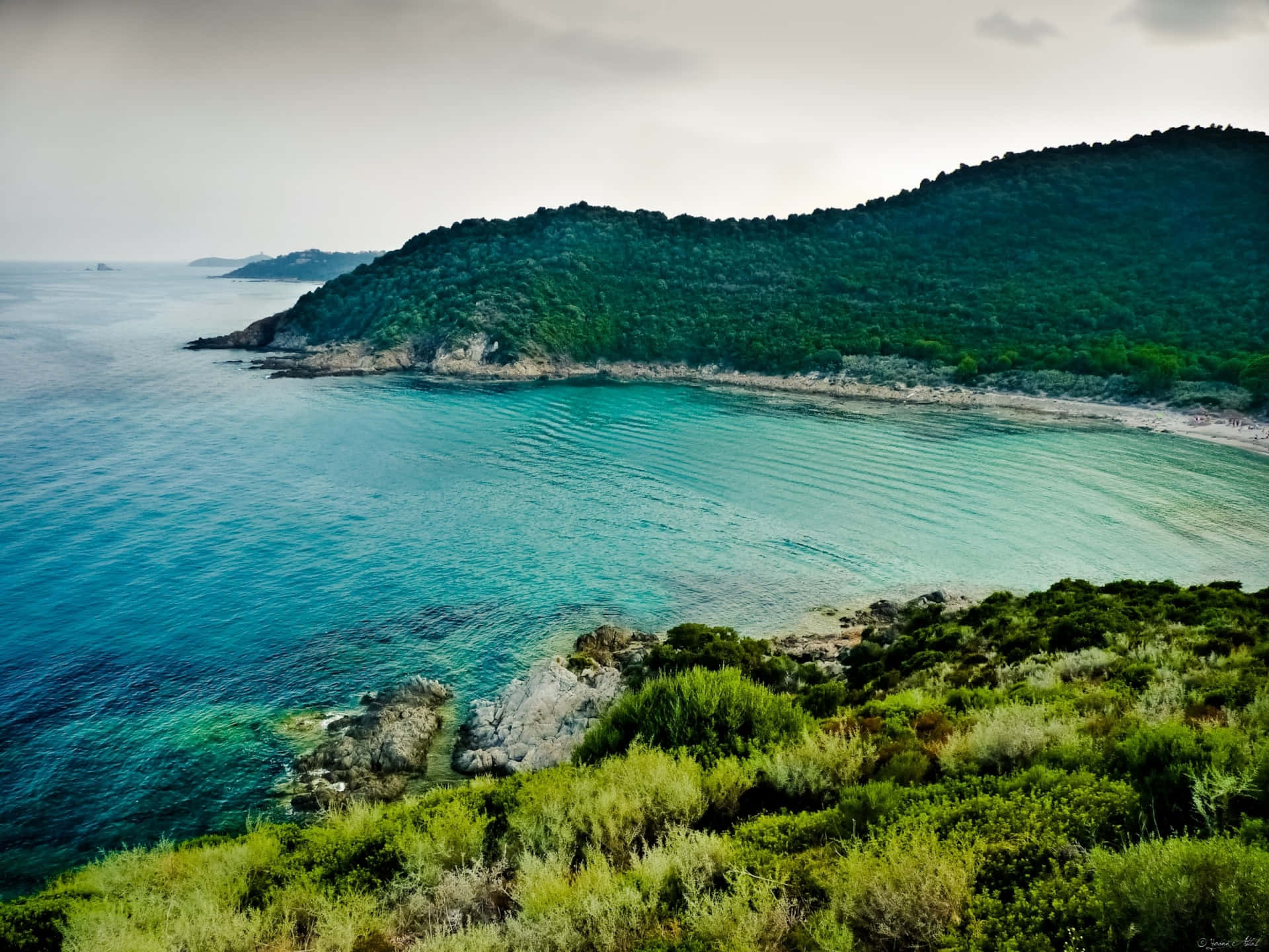 海岸海灣，碧綠海水和綠色山丘，多雲天空