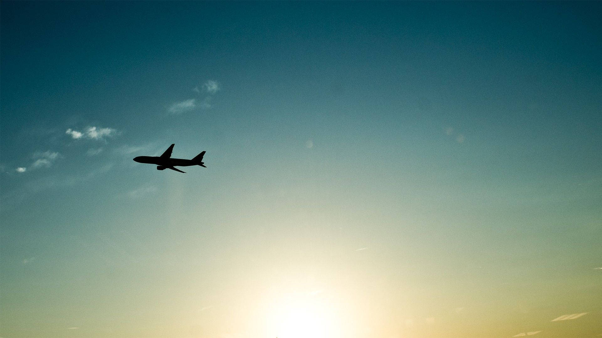 翱翔天際：一架小型黑飛機高飛於晴空 壁紙 — 孤獨的飛機剪影在漸變的天空中翱翔，天空閃爍著夕陽的色彩。