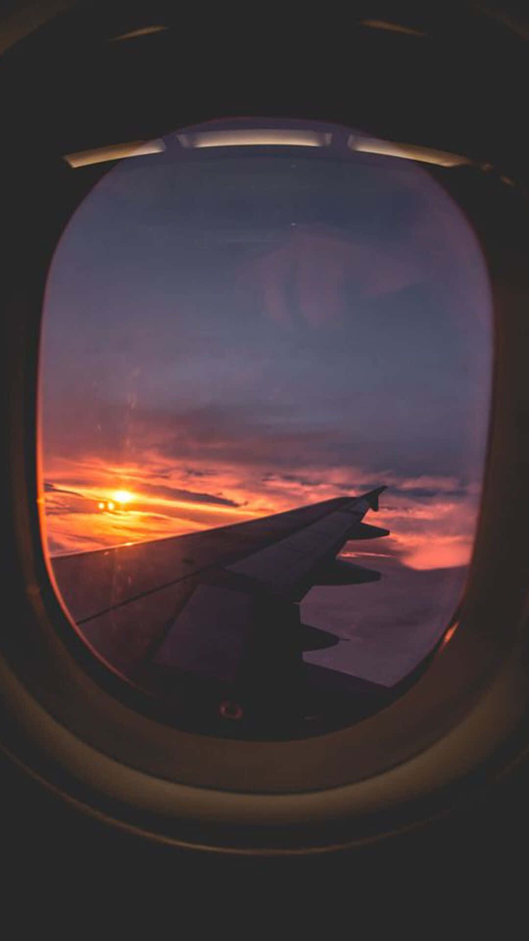 翱翔雲層之上 壁紙 — 透過飛機窗戶看到的機翼剪影，背景是火紅的日落。