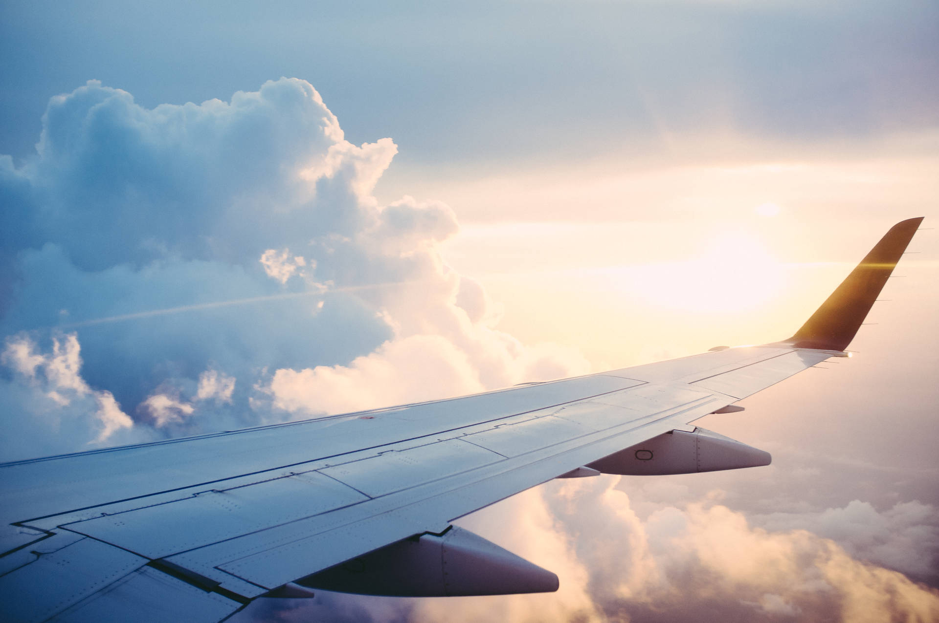 飛機機翼在金色夕陽中翱翔於雲層之上