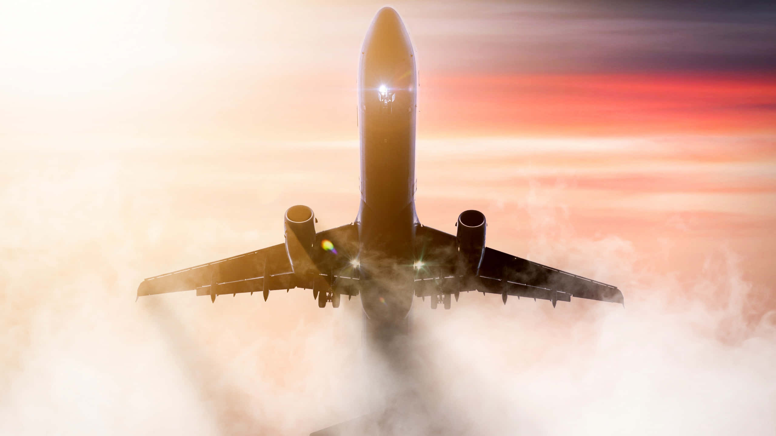 翱翔雲端，自由無限 壁紙 — 一架商用飛機在日落時翱翔於雲層之上，引擎發光，天空呈現火熱的橙色。