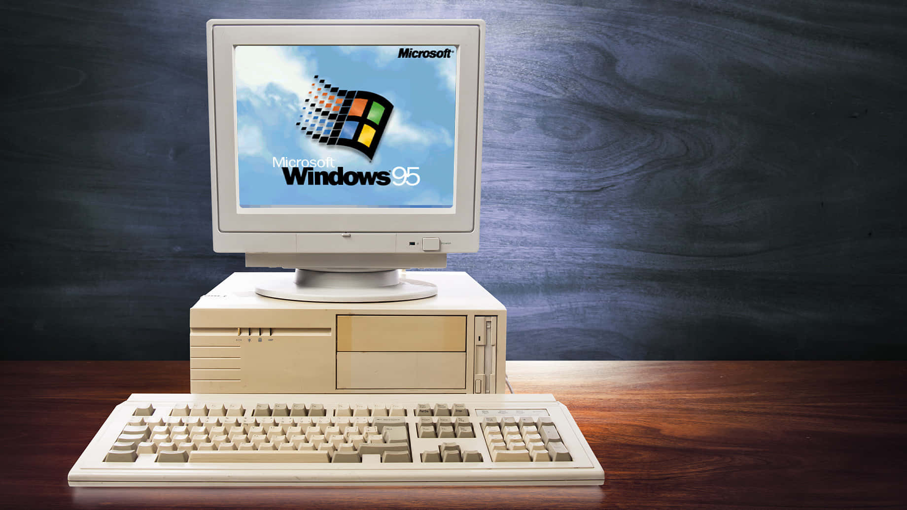 在深色木牆前的木質書桌上，復古米色 Windows 95 電腦設置。