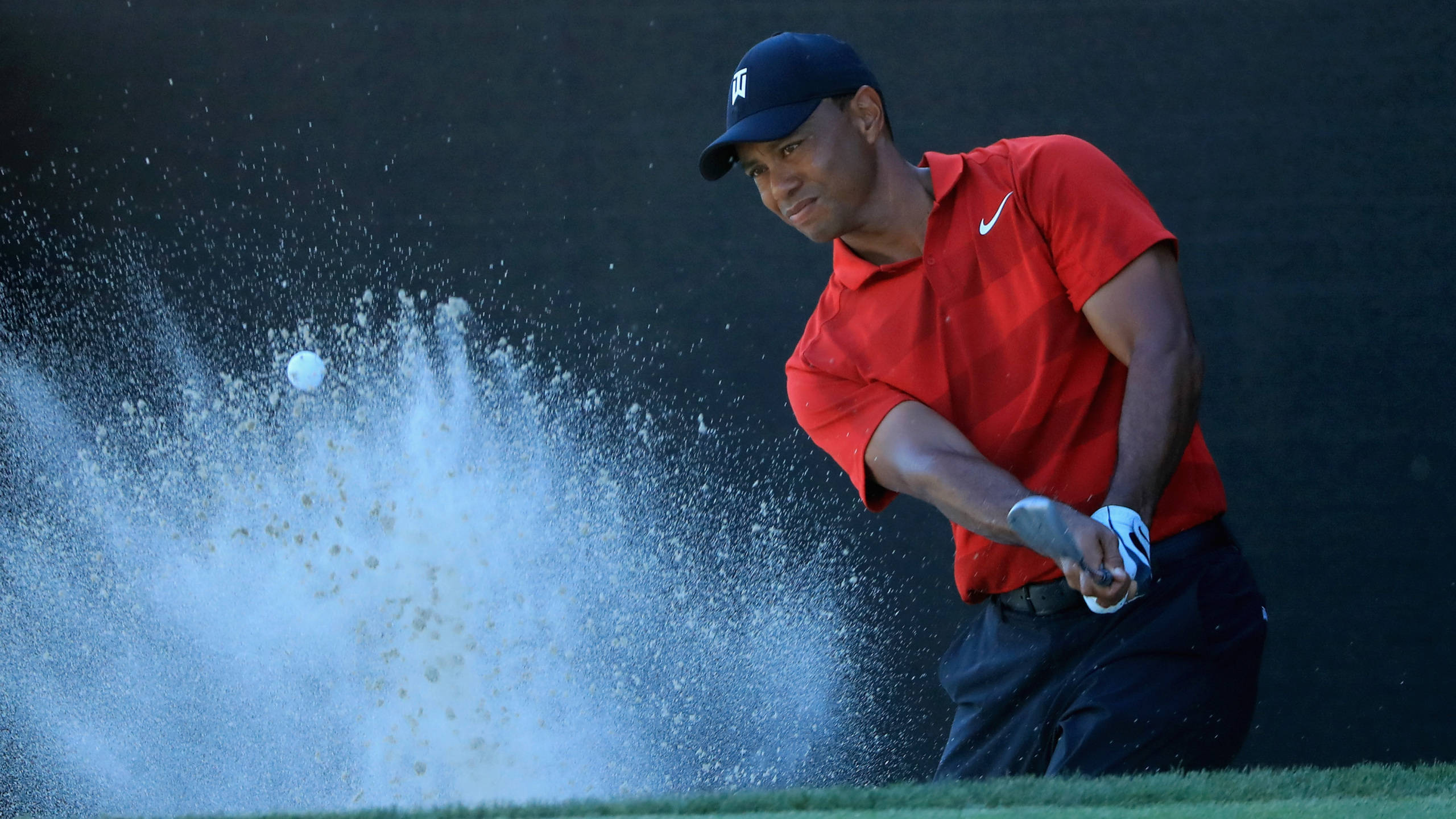 woods 桌布 壁紙 — 老虎活士揮動球桿，將高爾夫球從沙坑中擊出，沙子戲劇性地在他身後飛濺。