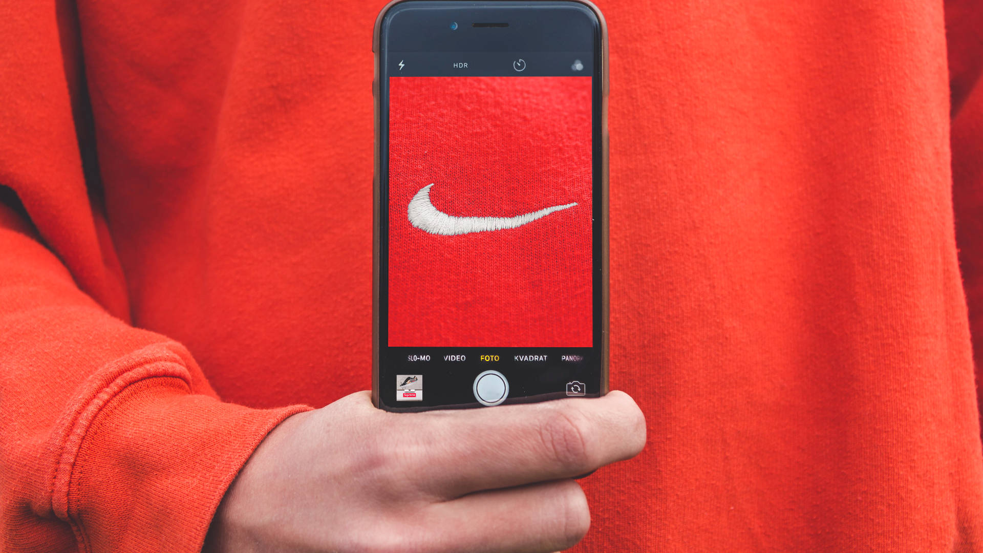 手拿著手機拍攝紅色布料上的Nike標誌。