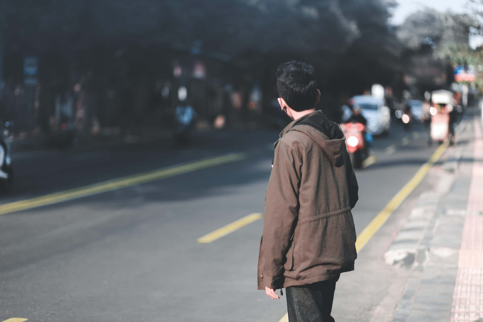 一個穿著棕色外套的人站在街道上，車輛駛過。