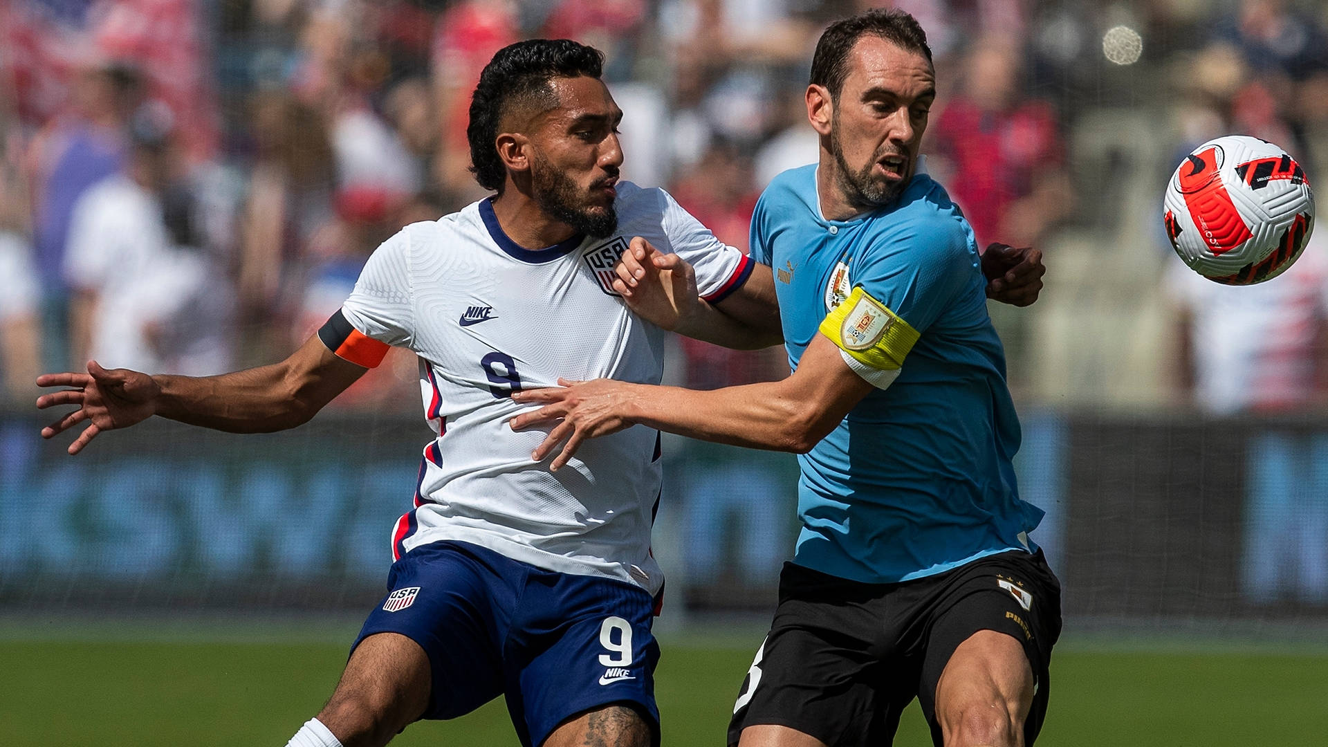 兩名男性足球運動員在陽光明媚的球場上爭球。