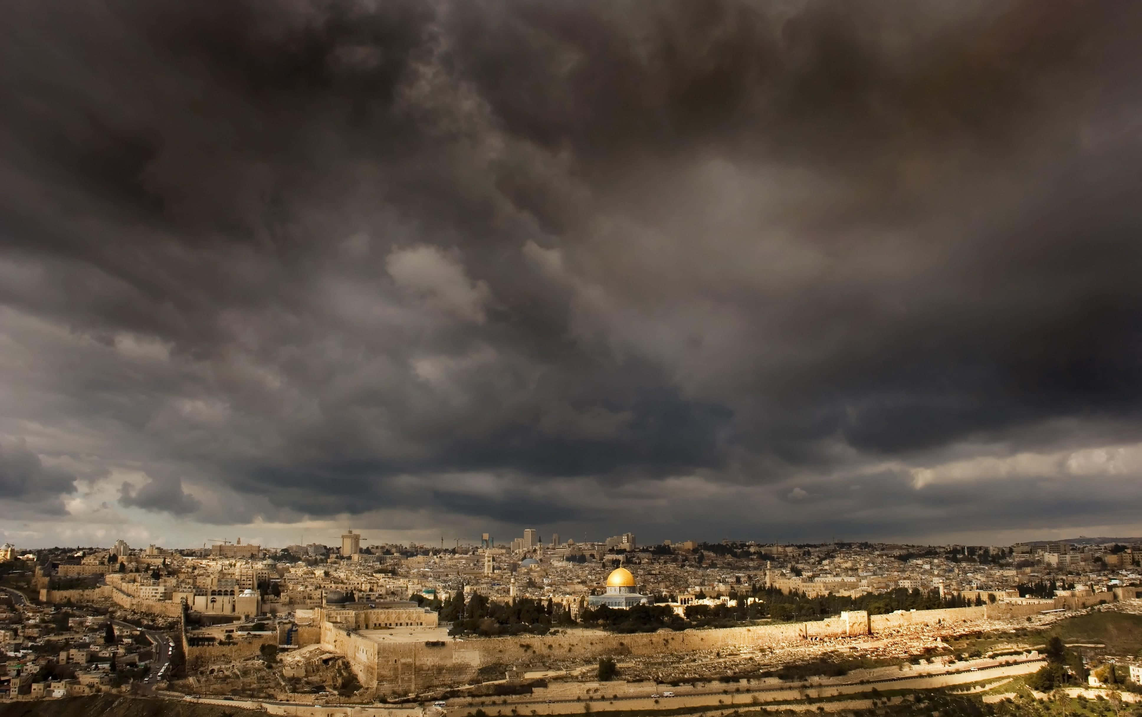 Israel 桌布 壁紙 — 耶路撒冷戲劇性的城市景觀，籠罩在陰沉的暴風雲層下，金色的圓頂清真寺在下方隱約發光。