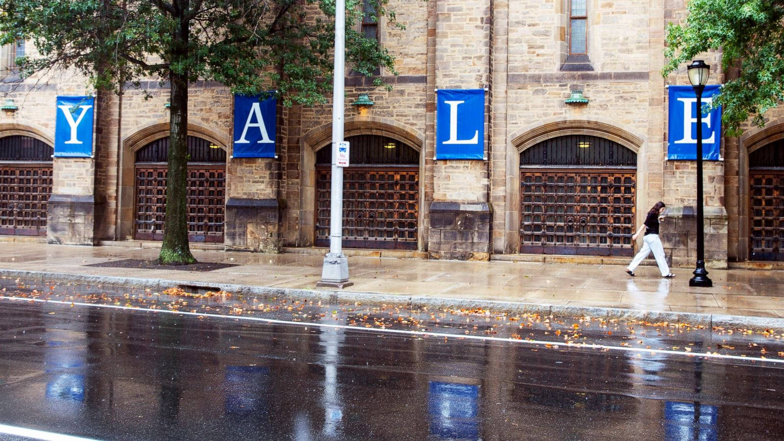 一個人在潮濕的秋雨天走過耶魯大學建築，路面濕滑。
