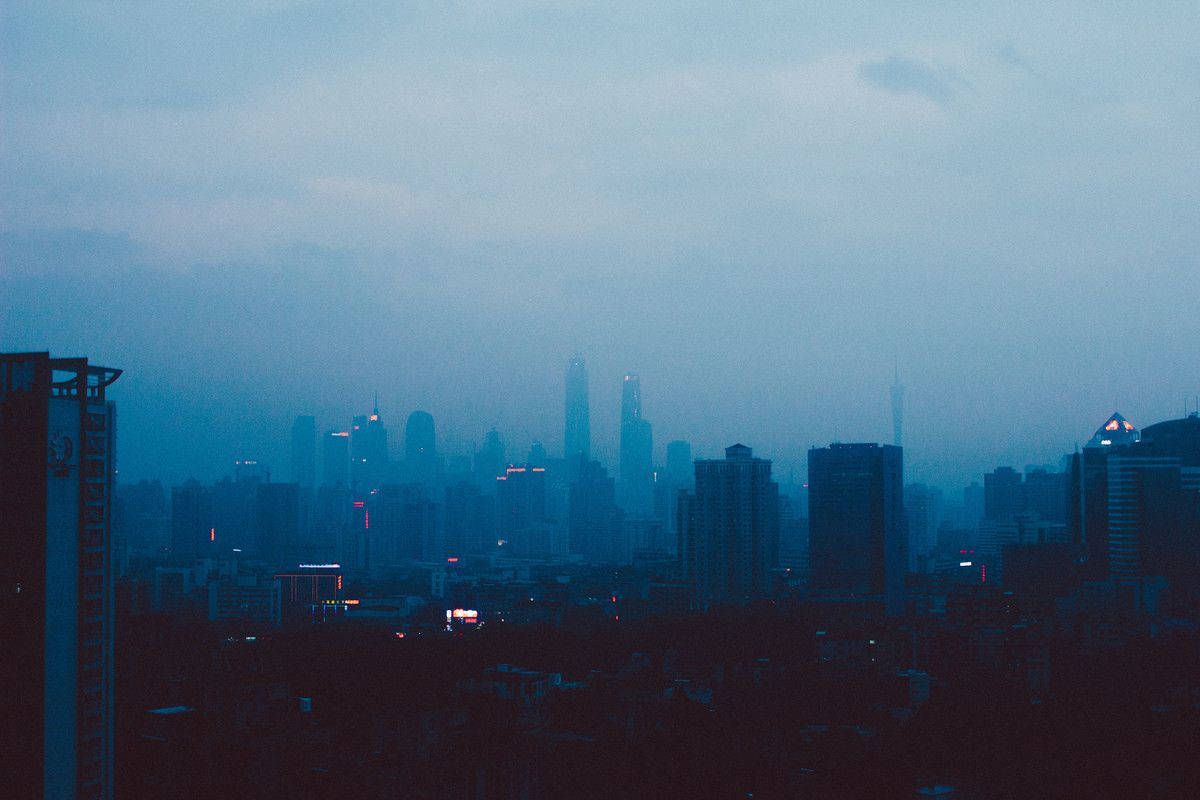 聆聽Lo-fi Hip Hop，調節心情與氛圍 壁紙 — 黃昏時分朦朧的城市天際線，帶有柔和的藍色調和建築物散發的零星紅光。
