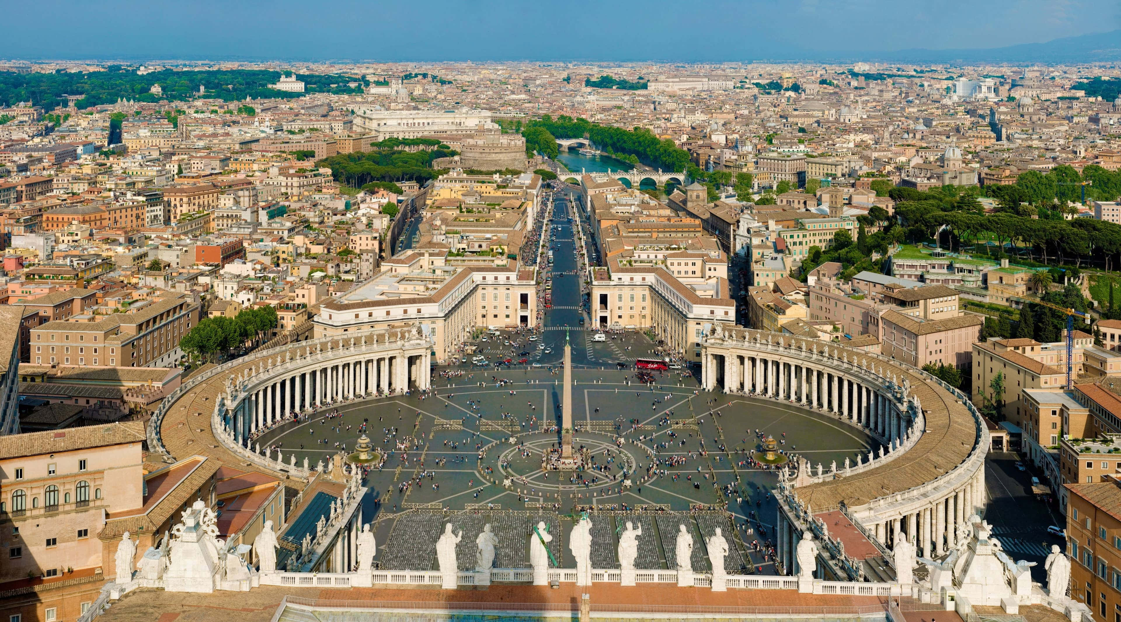 Rome 桌布 壁紙 — 聖伯多祿廣場的鳥瞰圖，擁有宏偉的柱廊和方尖碑，周圍是梵蒂岡城繁忙的屋頂，天空清澈湛藍。