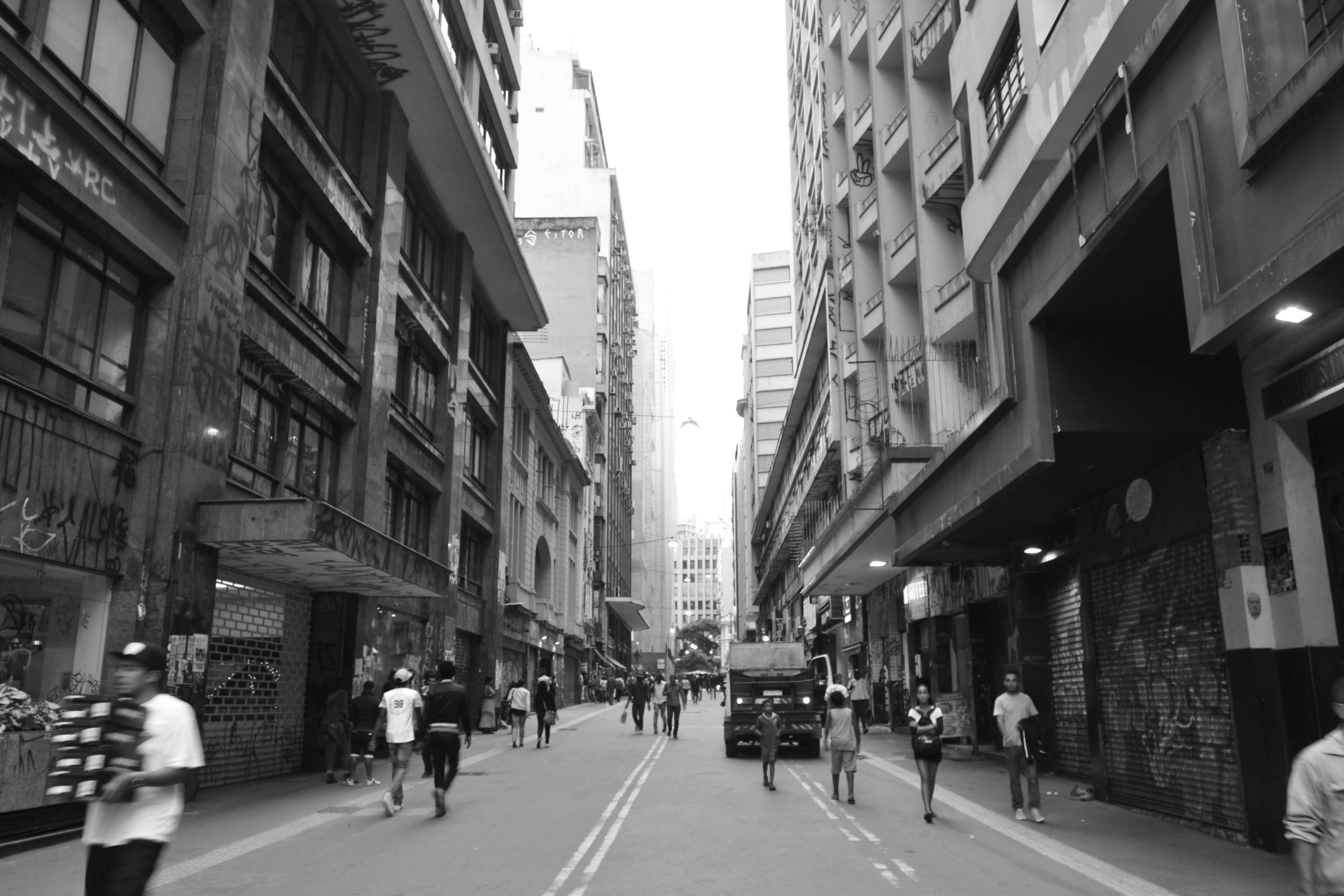 聖保羅巴西步行街 壁紙 — 一條繁忙的黑白城市街道，行人和一輛卡車在有塗鴉的高樓之間穿梭。