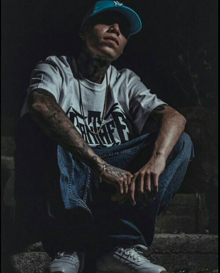 戴帽子和牛仔褲的紋身男子在昏暗光線下坐在石階上。