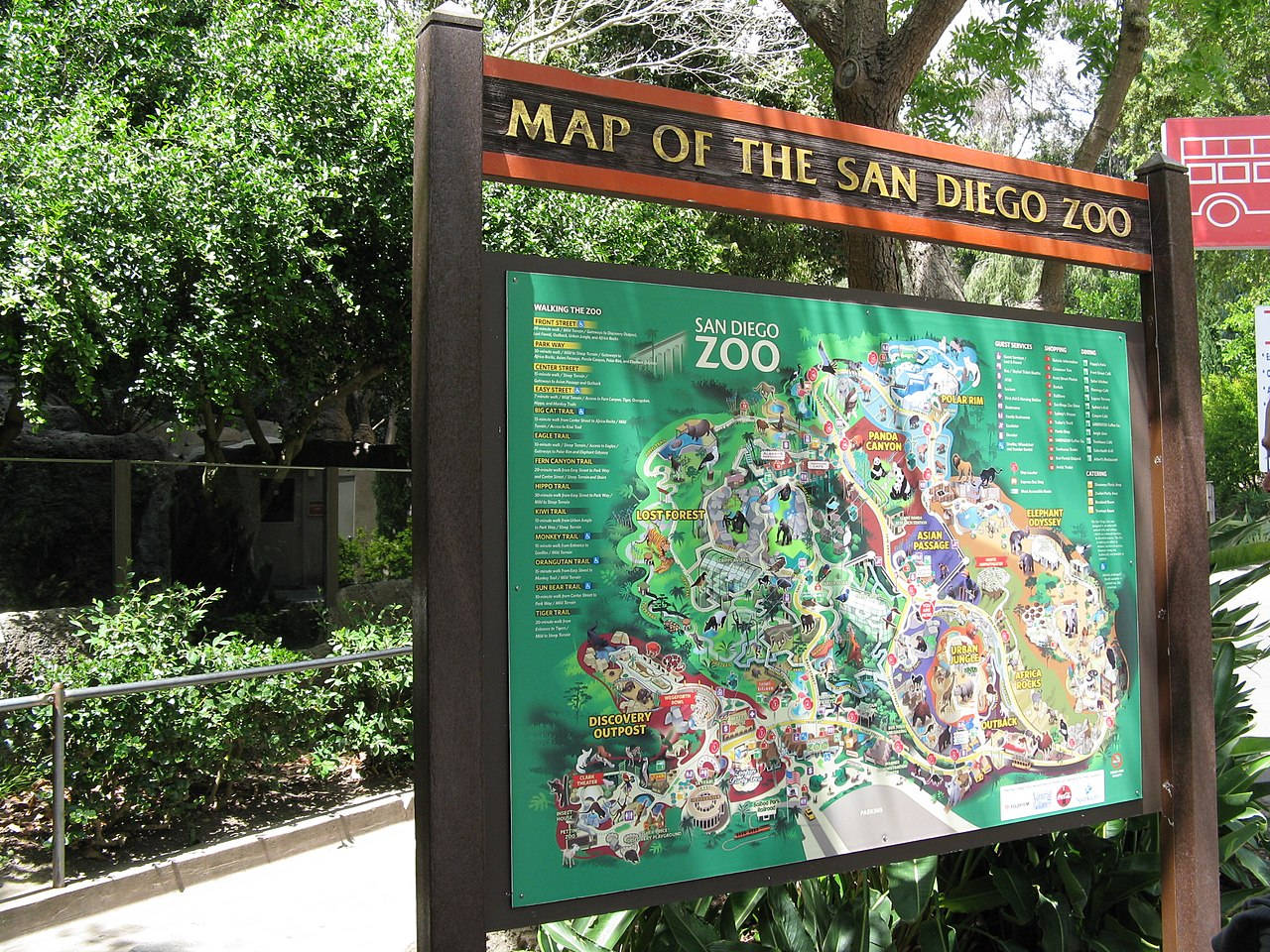 在陽光明媚的公園環境中，一個充滿活力的動物園地圖標誌被綠樹環繞。