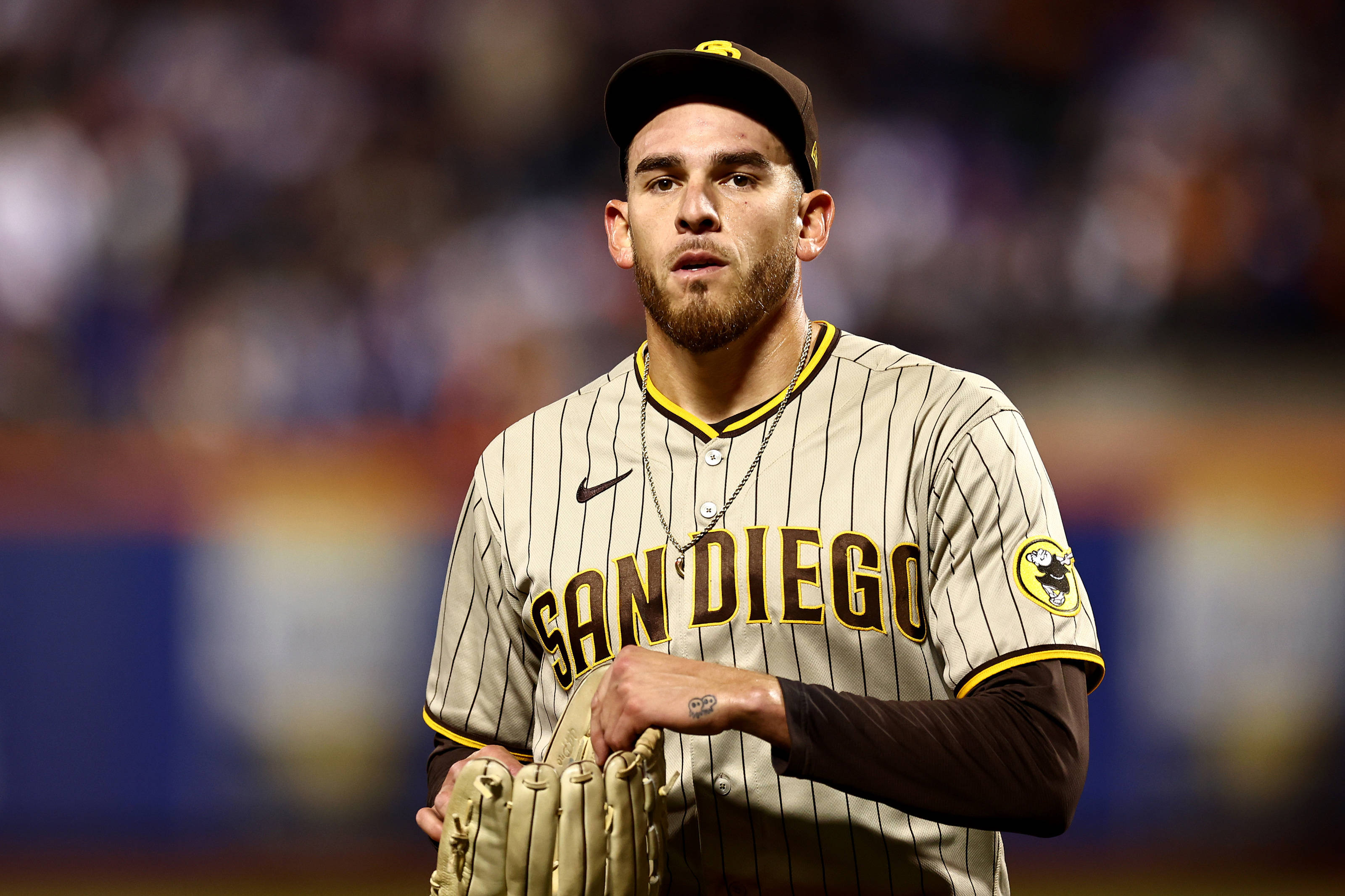 聖地牙哥教士隊 Joe Musgrove 棒球投手 壁紙 — 一位專注的聖地牙哥教士隊棒球運動員穿著細條紋制服，在球場燈光下握著手套。