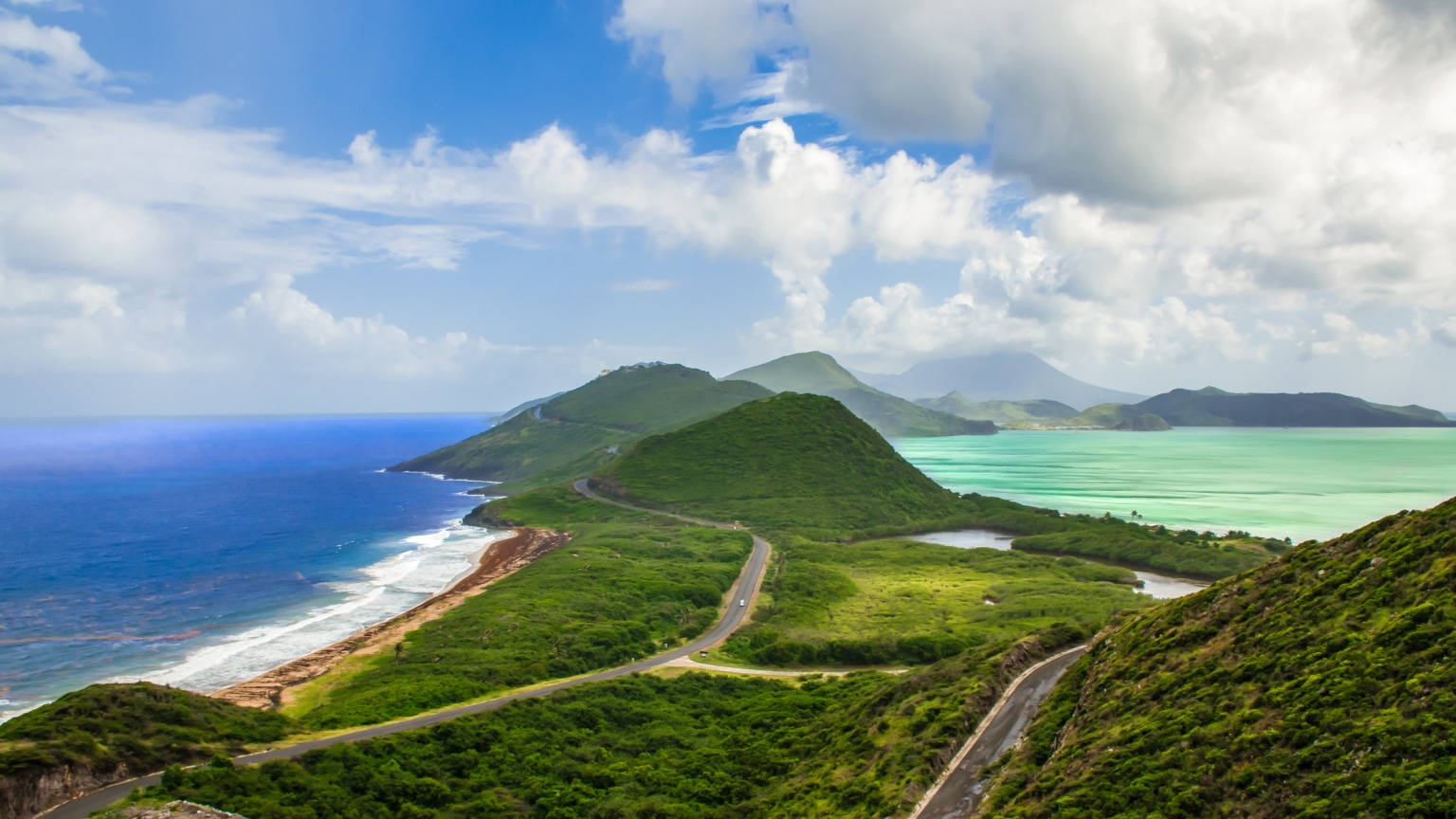 海岸公路蜿蜒穿過綠色山丘，旁邊是碧綠的海洋，藍天白雲
