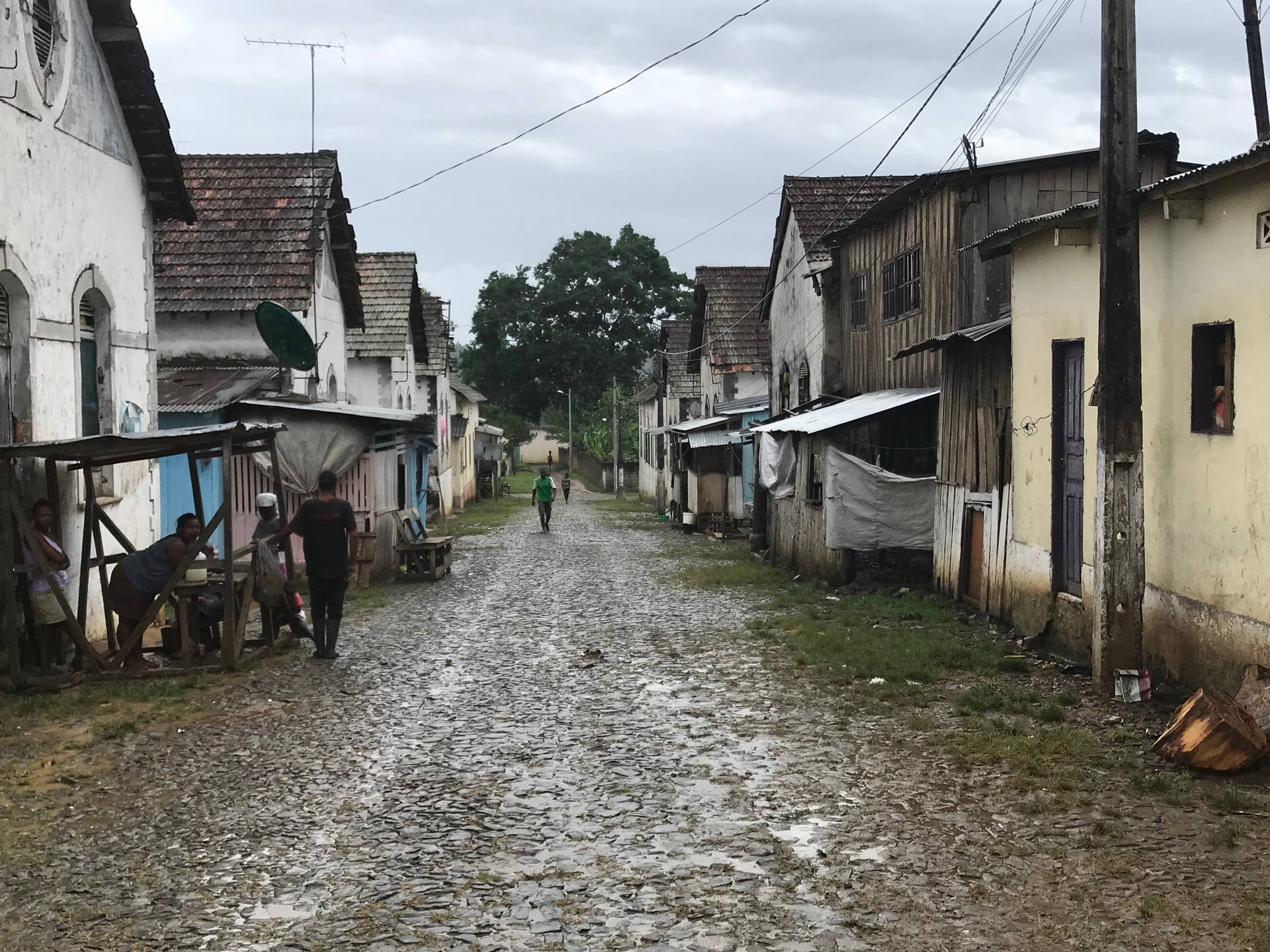 潮濕的鵝卵石街道，有行人和棚屋，位於貧困的城市社區。
