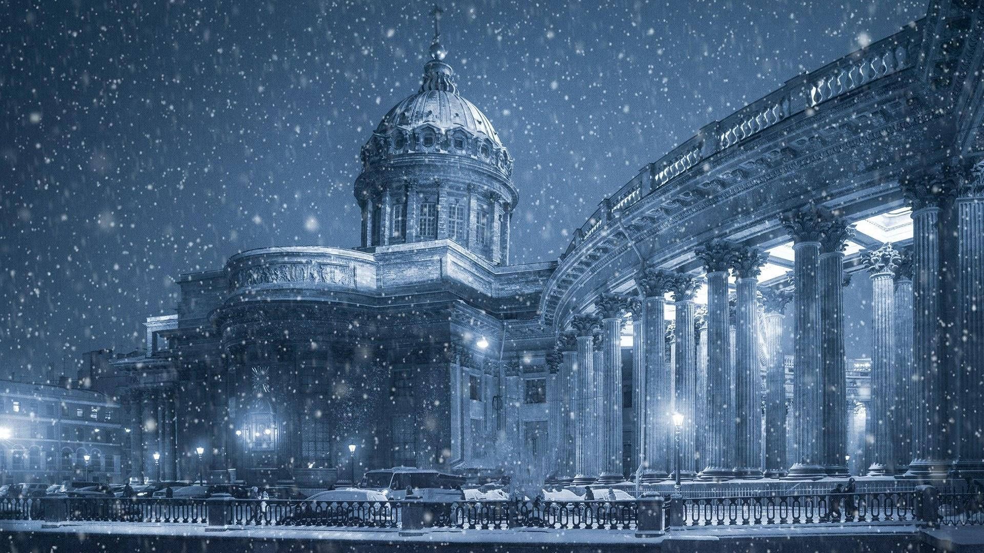 聖彼得堡雪夜風景 壁紙 — 雪花在夜空中飄蕩，飄過一座宏偉的新古典主義建築，建築物有發光的燈光和積雪的柱子。