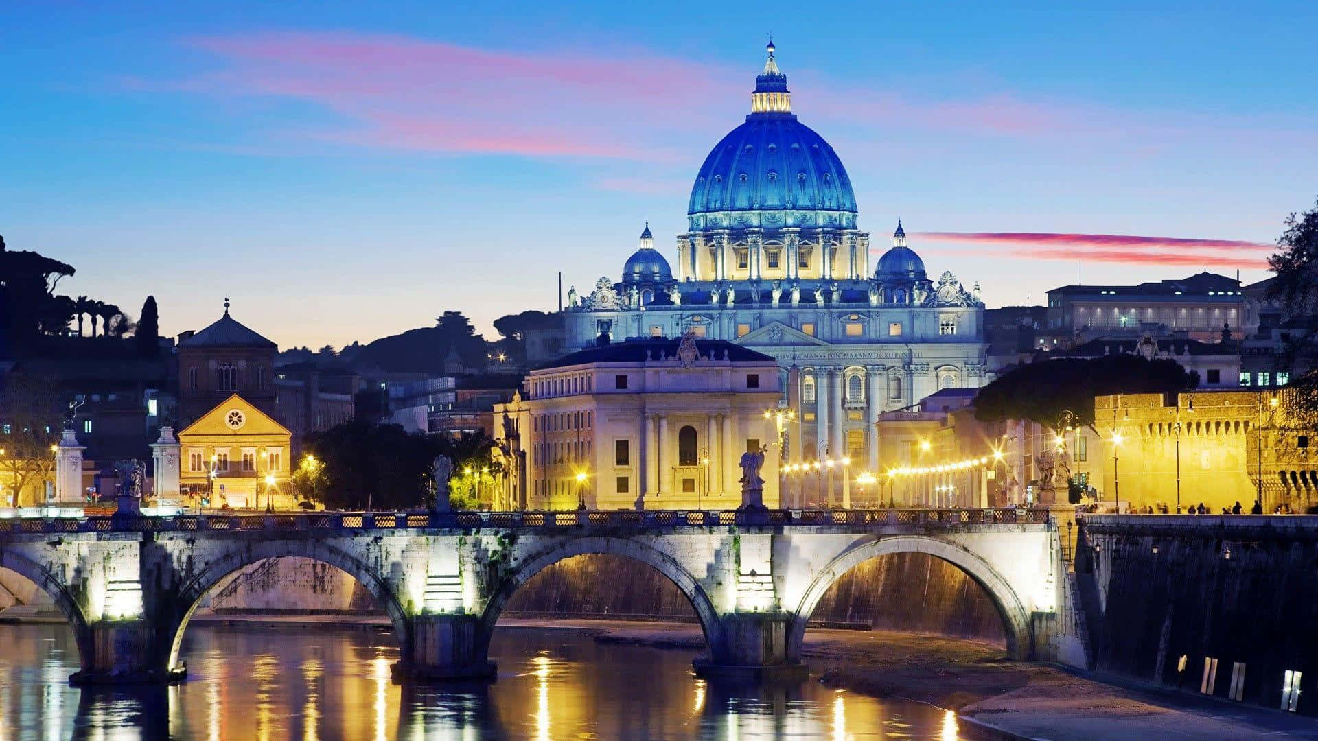 Rome 桌布 壁紙 — 聖彼得大教堂在黃昏時分被照亮，其標誌性圓頂在台伯河上的石橋上方發出藍色光芒。