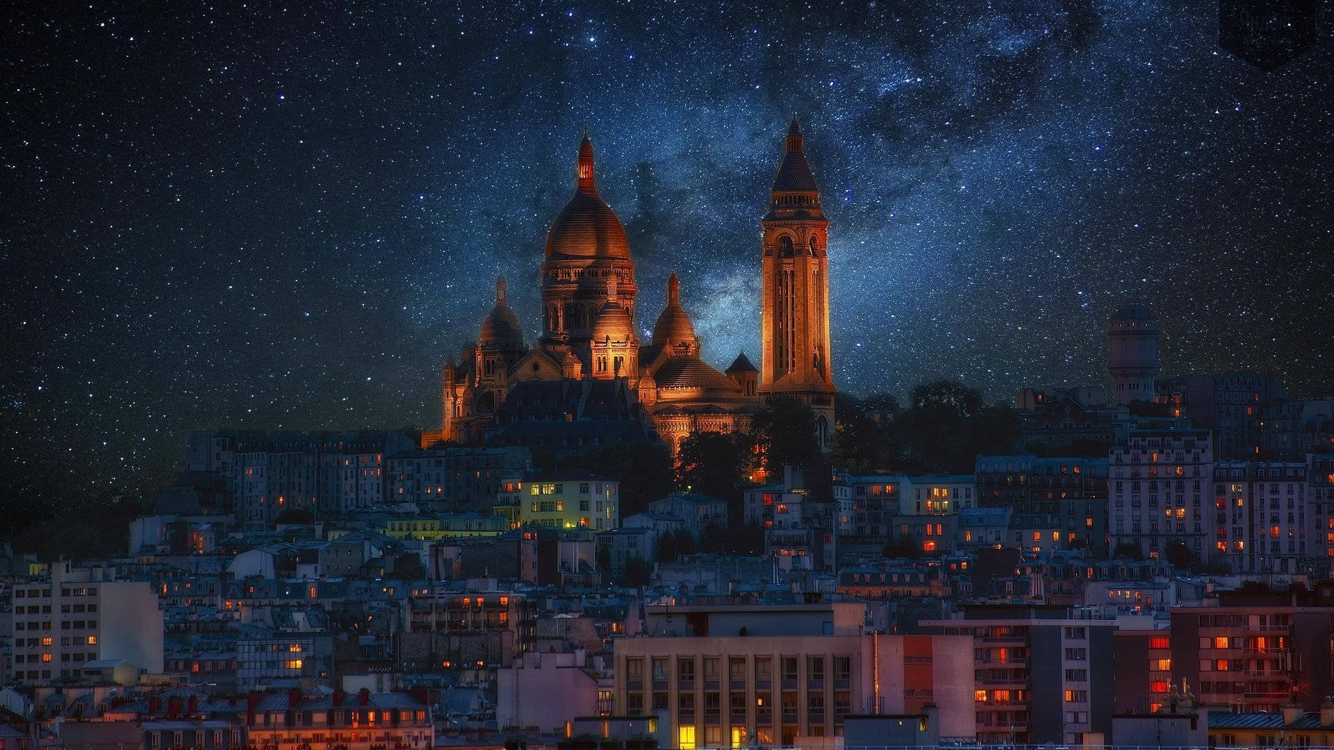 聖心大教堂星空夜景 壁紙 — 聖心大教堂在繁星點點的夜空下溫暖地發光，銀河在巴黎城市景觀上方拱起。