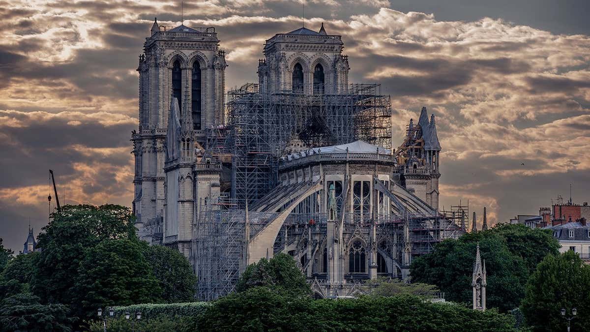 Gothic Architecture 桌布 壁紙 — 聖母院大教堂在戲劇性的暮色天空下矗立，廣泛的腳手架覆蓋其受損的屋頂和尖塔。