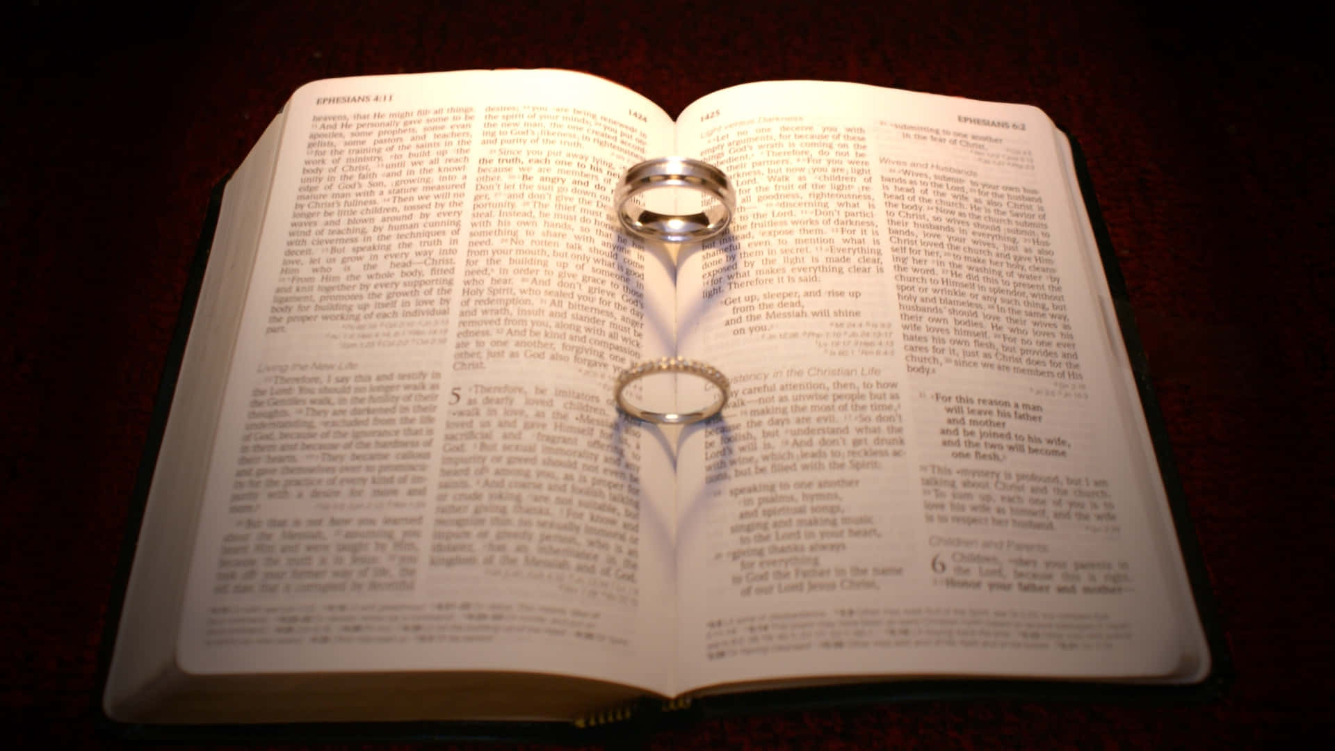 兩枚金色結婚戒指放在打開的聖經頁面上，溫暖燈光。
