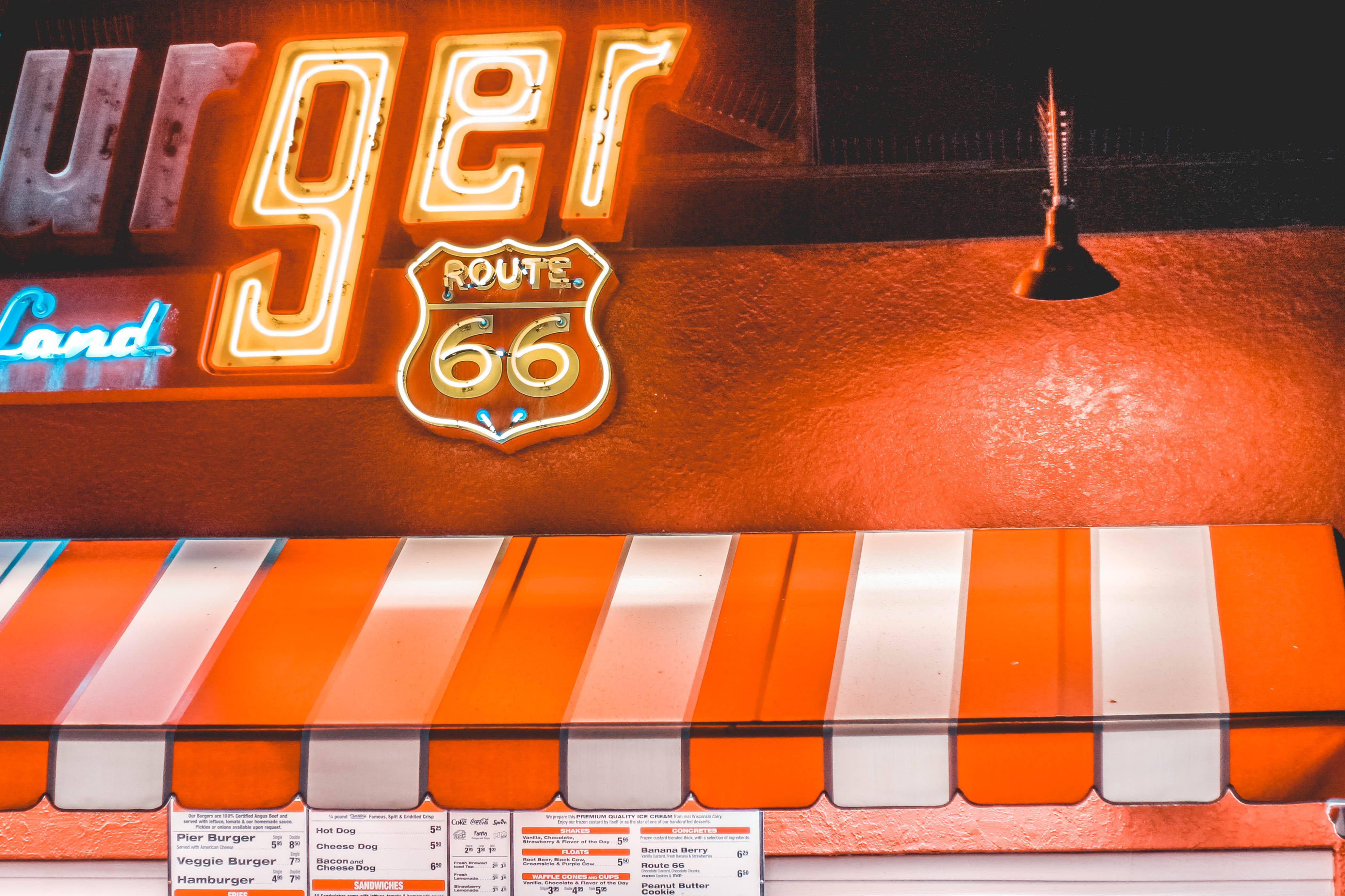 聖莫尼卡66號公路霓虹招牌 壁紙 — 一個發光的Burger Land霓虹招牌，帶有66號公路標誌，夜間照亮橙色簷篷和菜單板。