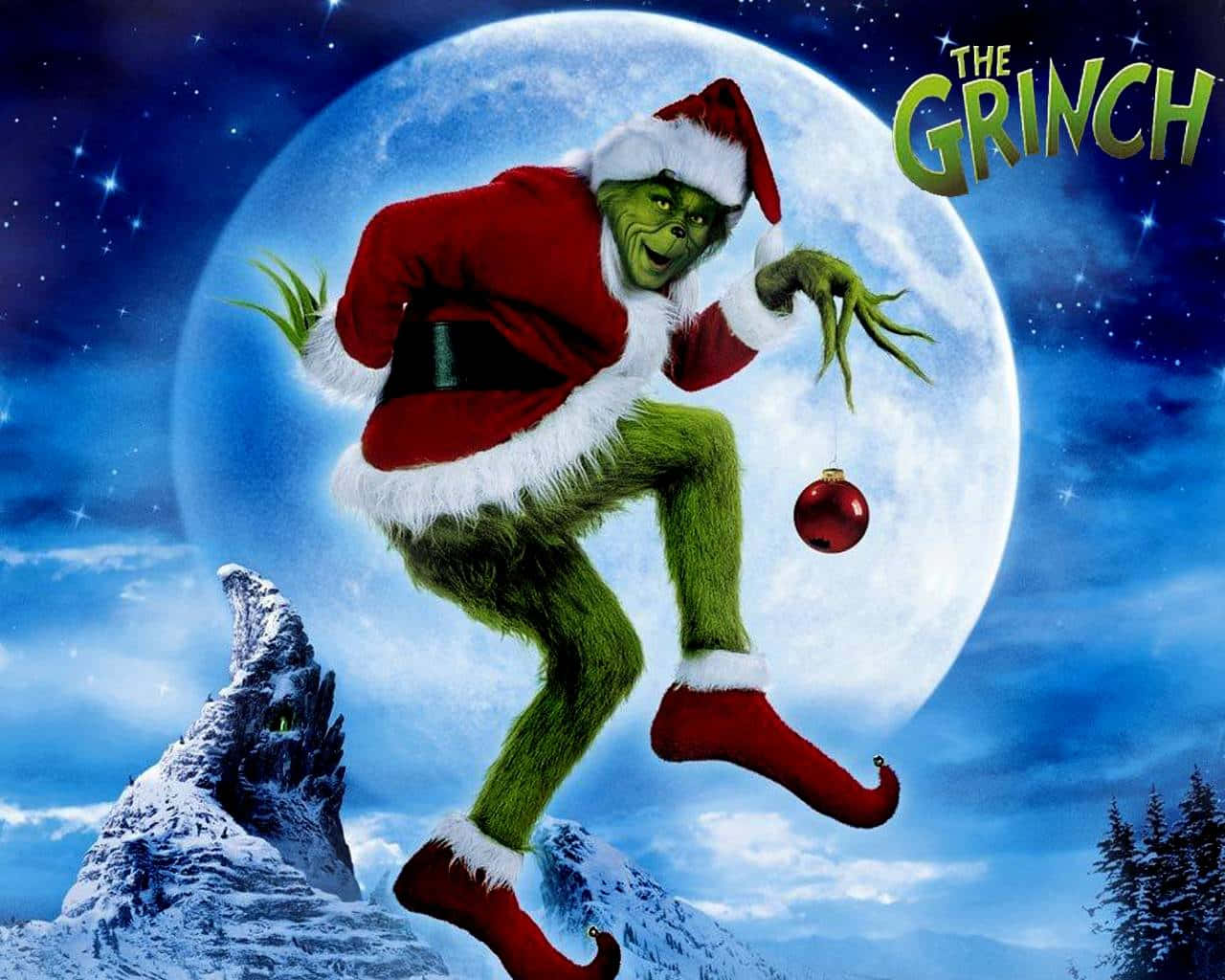 Christmas Movie 桌布 壁紙 — 聖誕怪傑穿著聖誕老人服裝，在雪山上對著巨大月亮歡快地跳躍，手持紅色裝飾球。