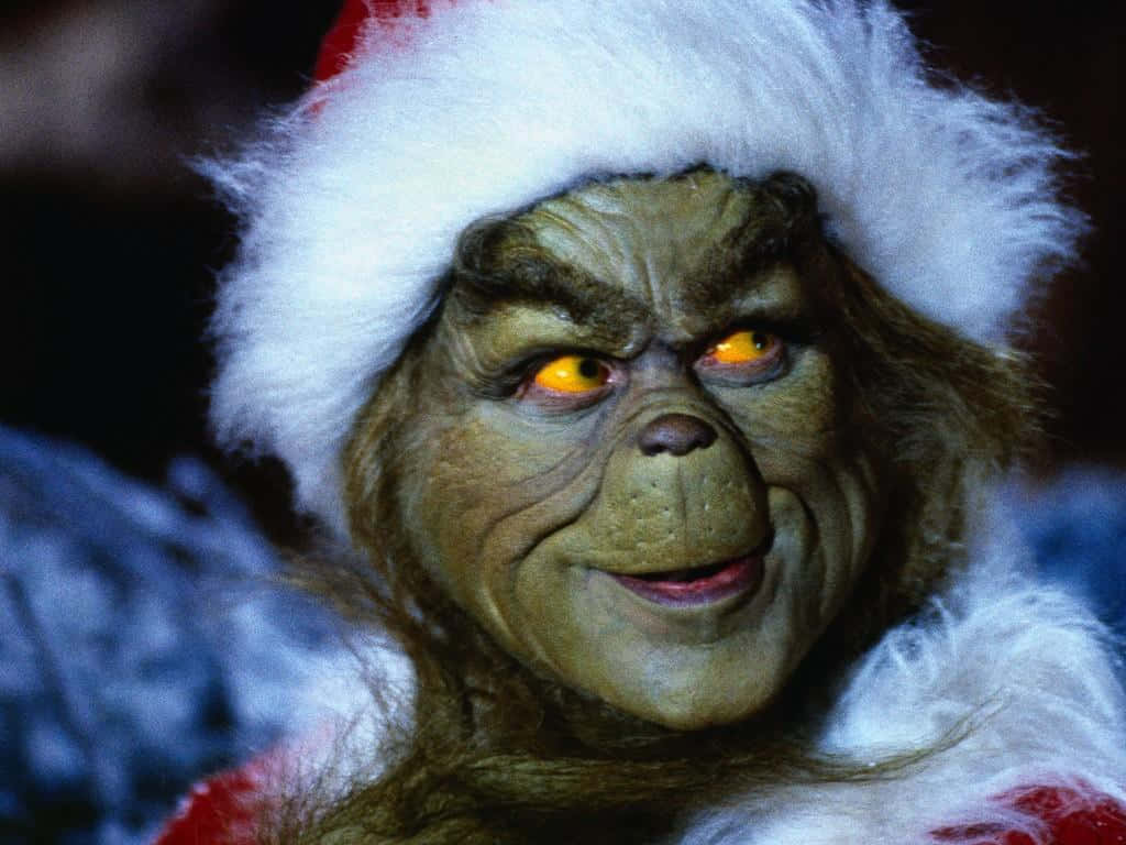 The Grinch 桌布 壁紙 — 聖誕怪傑近照，戴著聖誕帽，橙色發光眼睛，露出邪惡笑容。