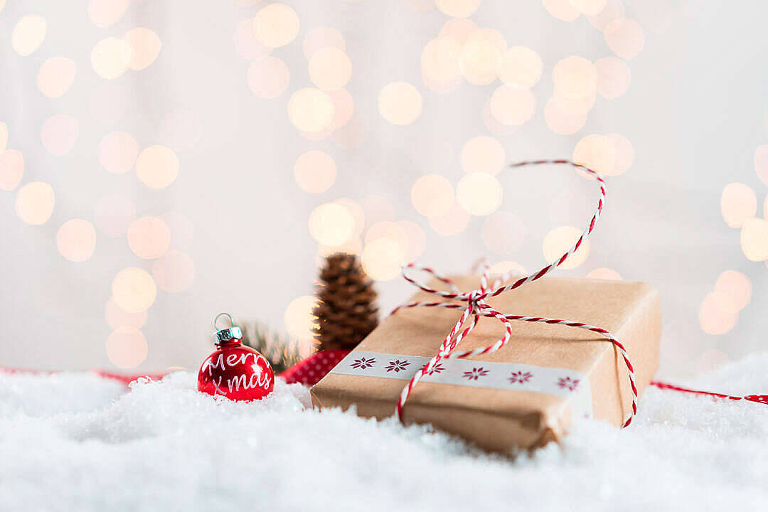 聖誕禮物與散景背景 壁紙 — 一份包裝好的禮物和紅色裝飾品放在雪白的絨毛中，溫暖的散景燈光在後面柔和地發光。