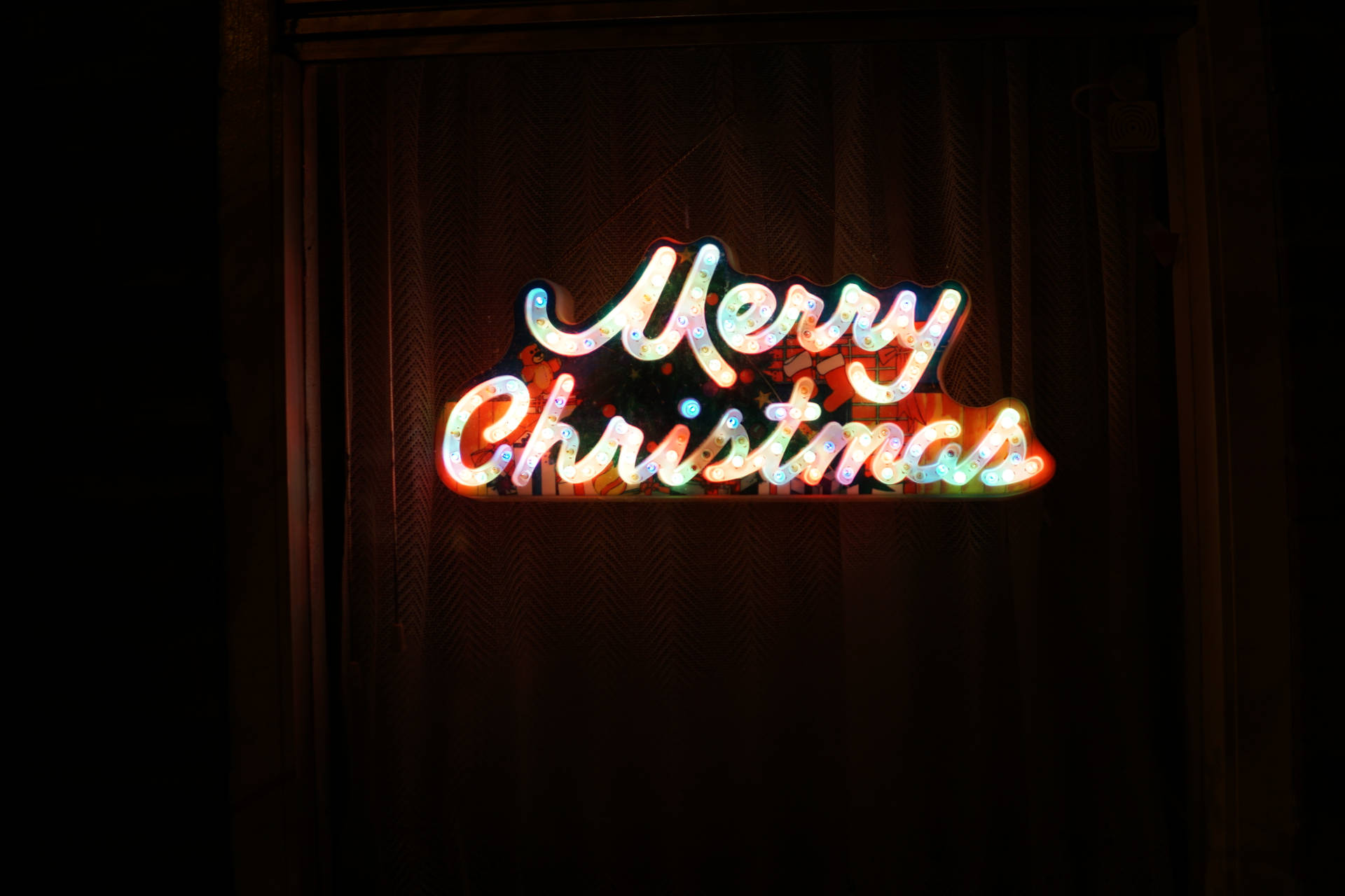 一個發光的霓虹燈牌在深色窗簾前顯示Merry Christmas。