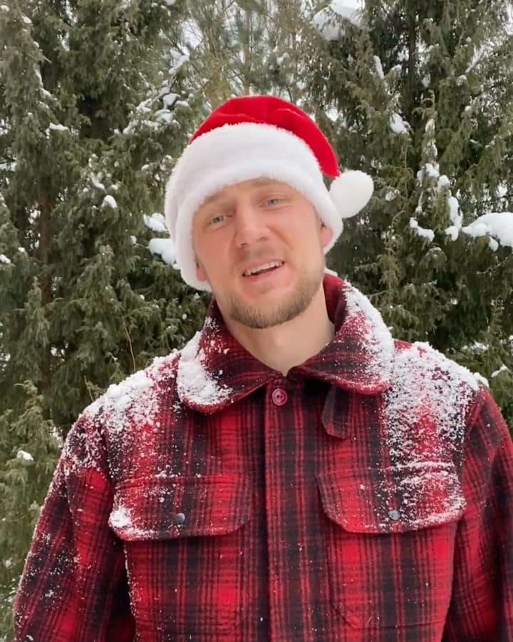 男人戴著聖誕帽和雪覆蓋的格仔外套，身處白雪覆蓋的松樹林。