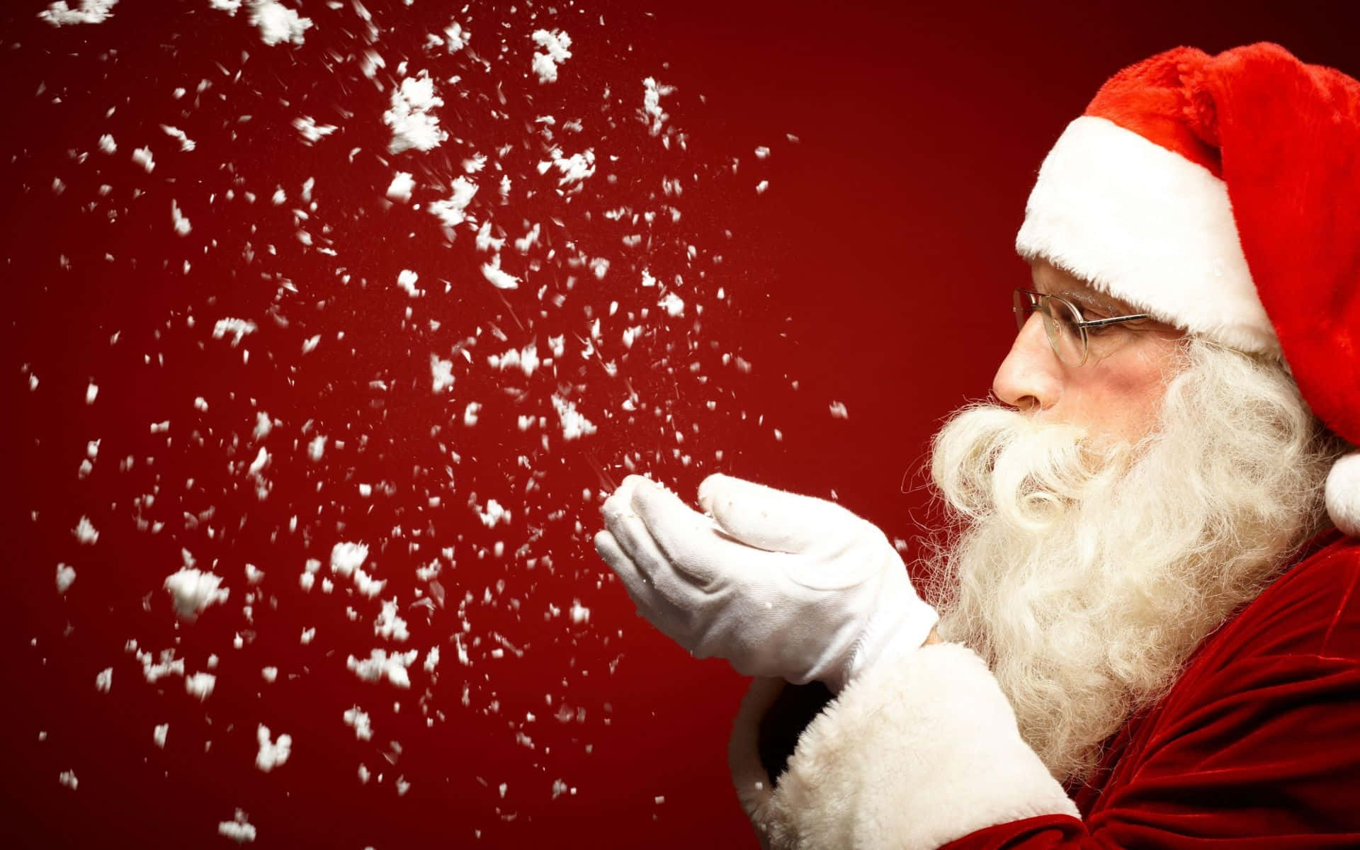 Santa Claus 桌布 壁紙 — 聖誕老人喺深紅色背景前，喺工作室拍攝中從手中吹出雪花。