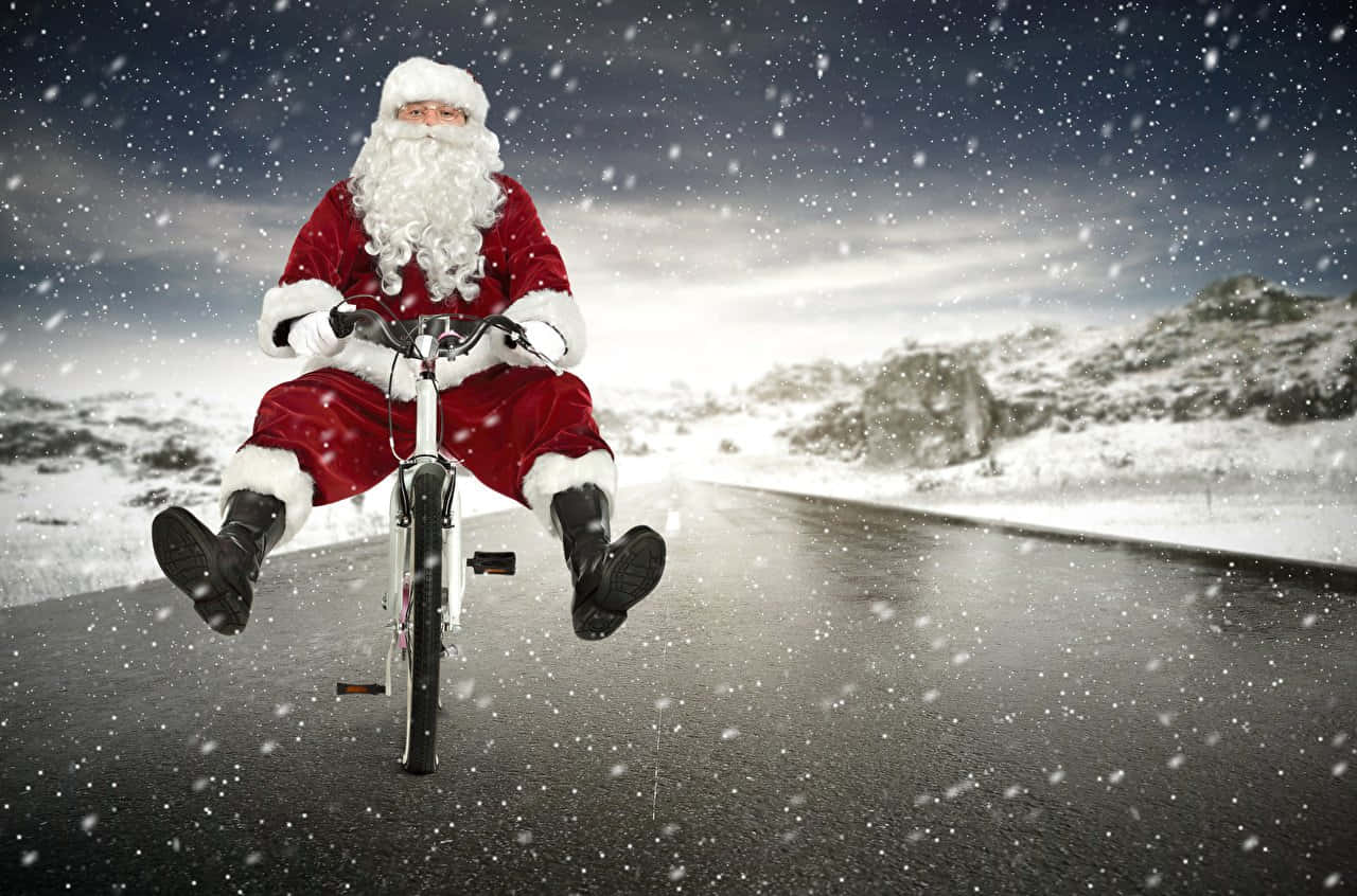 搞笑聖誕gif 桌布 壁紙 — 聖誕老人在飄雪中沿著積雪的道路騎單車，背景是白雪覆蓋的山丘。