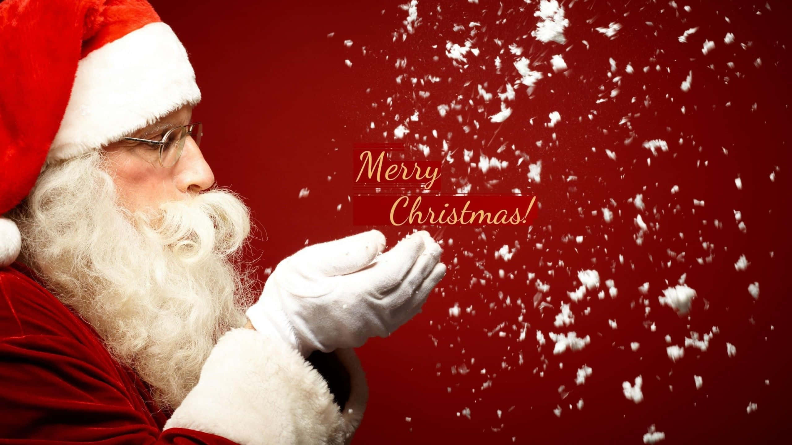 Santa Claus 桌布 壁紙 — 聖誕老人從戴手套的雙手中吹出雪花，背景為濃郁的紅色，並帶有「Merry Christmas!」文字。