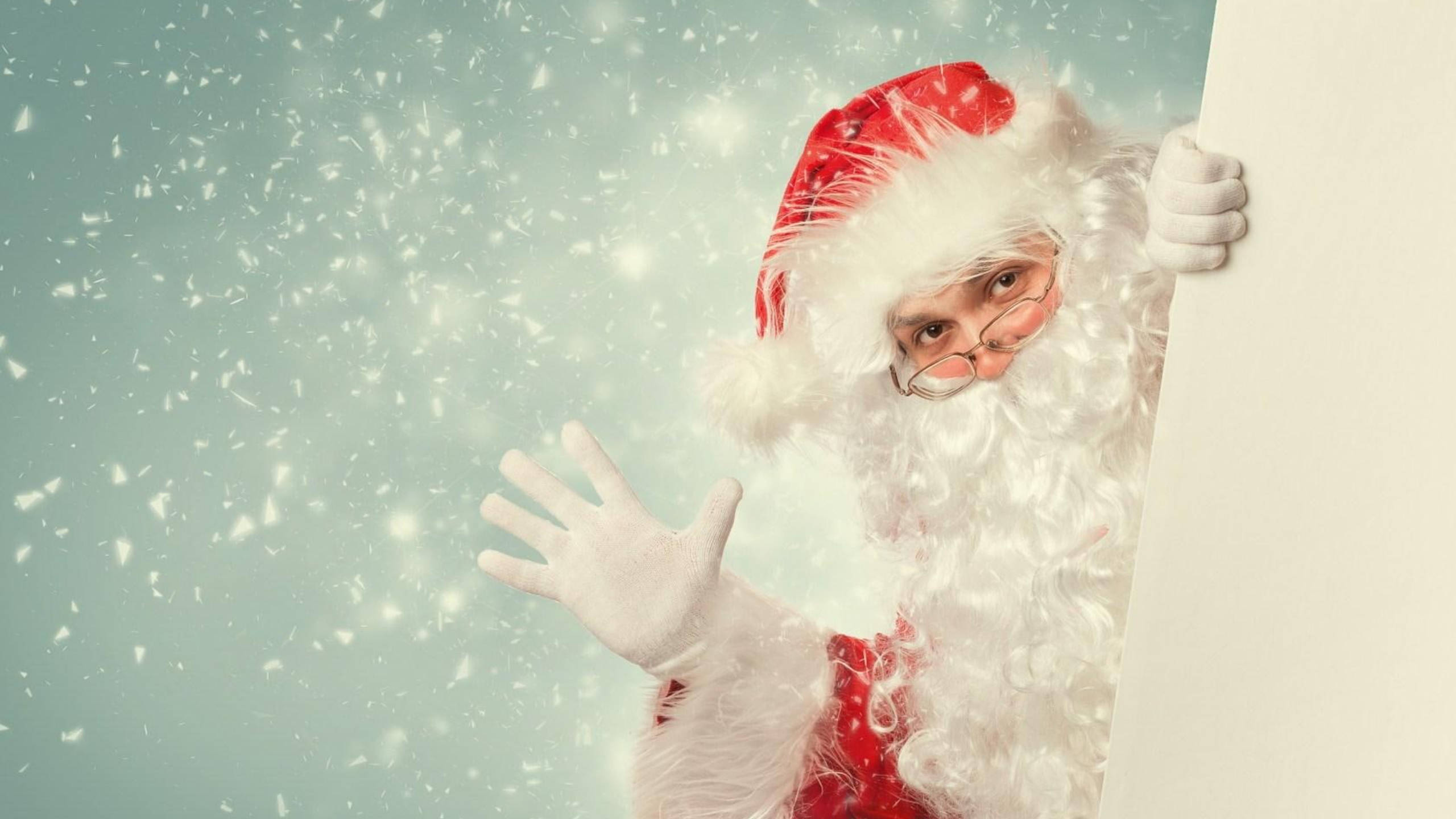 Waving Santa Claus In Snow 壁紙 — 聖誕老人從白色板後探出頭來，雪花在柔和的青綠色背景中飄落。