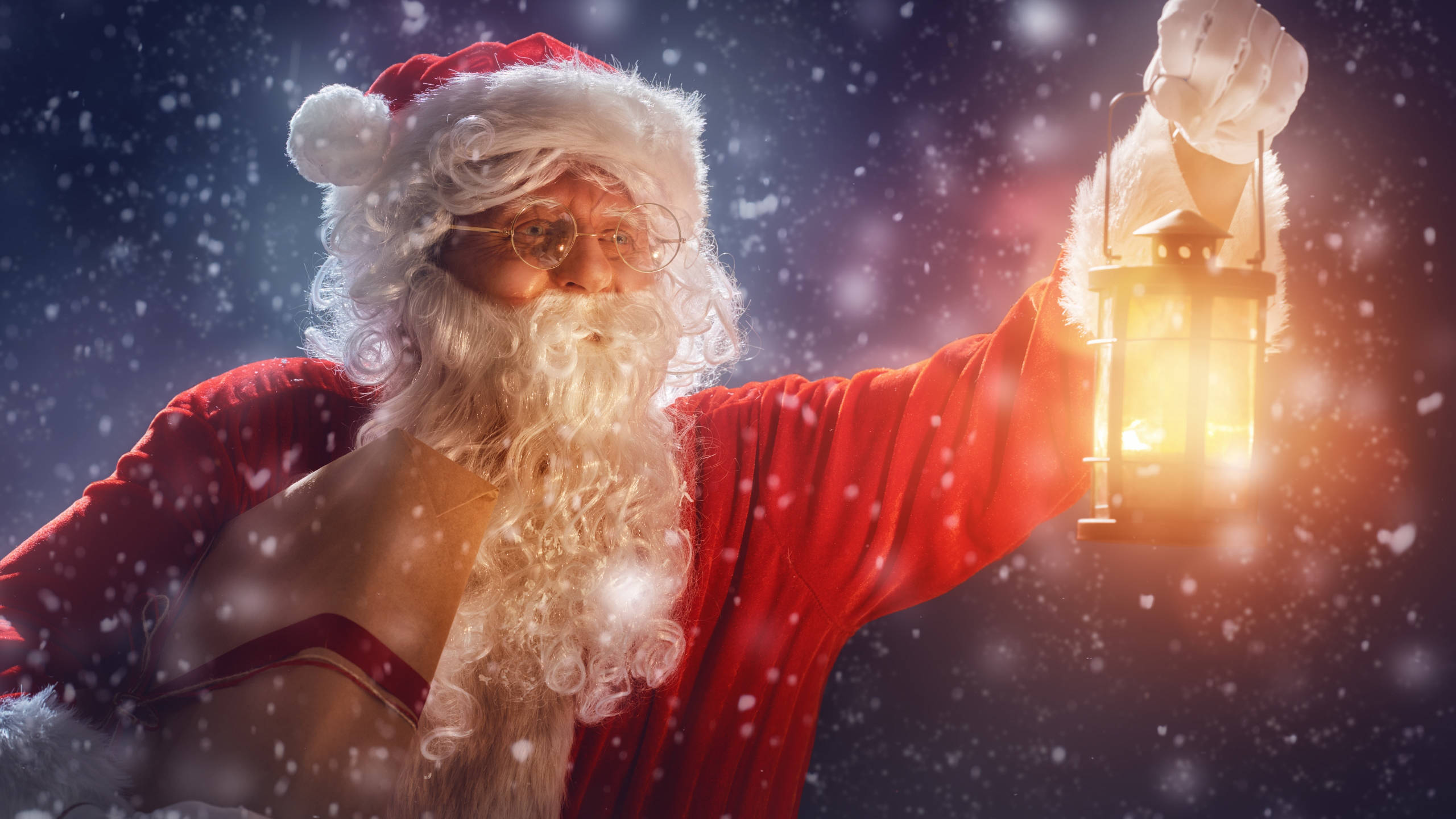 Santa Claus With Lantern 壁紙 — 聖誕老人穿著紅色西裝，在黑暗星空下雪花飄落時手持發光燈籠。