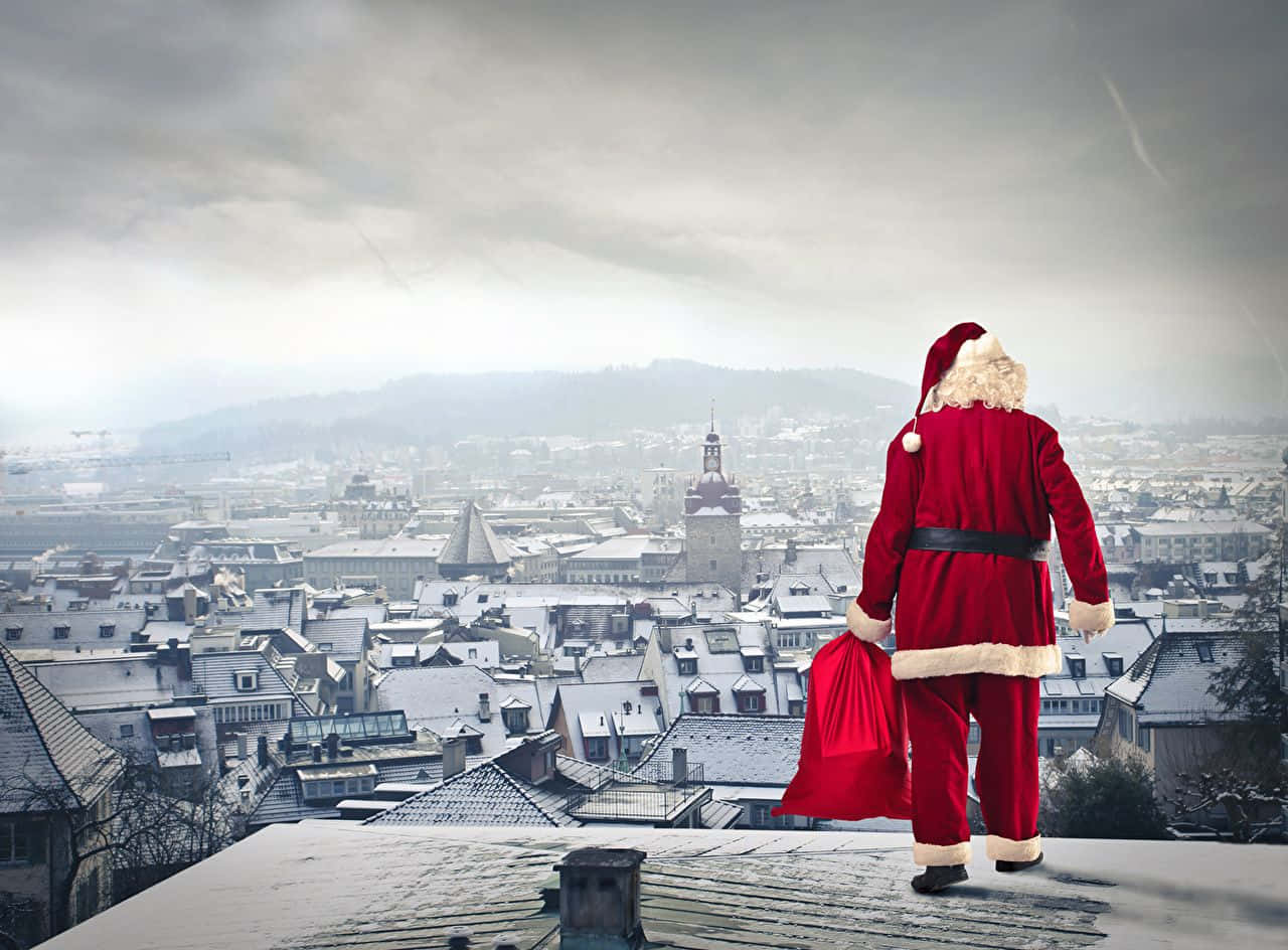 Santa Claus 桌布 壁紙 — 聖誕老人站在積雪的屋頂上，俯瞰灰色天空下的冬日城市景觀。